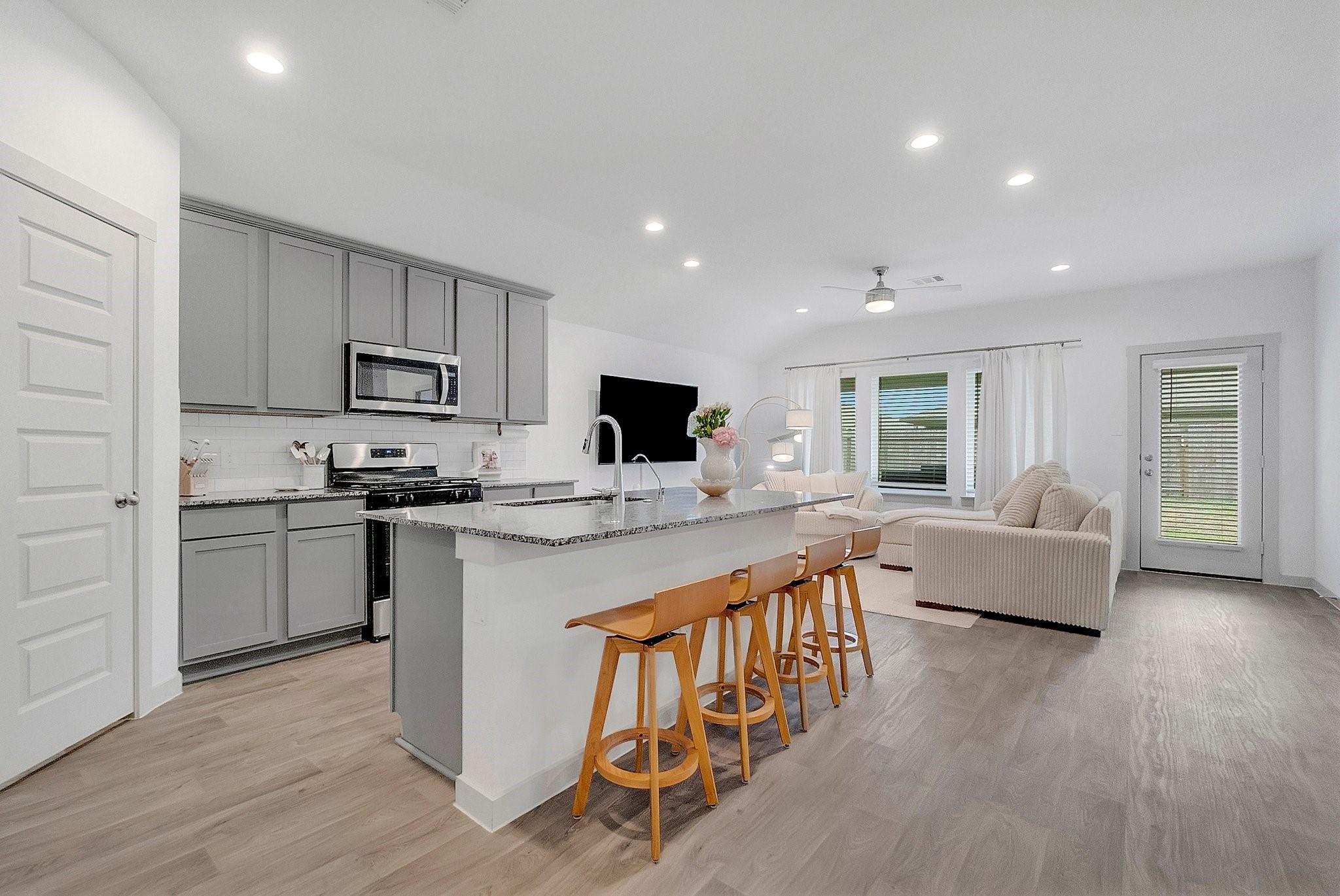 Open kitchen and living room with a large island, bar stools, and gray cabinetry.
