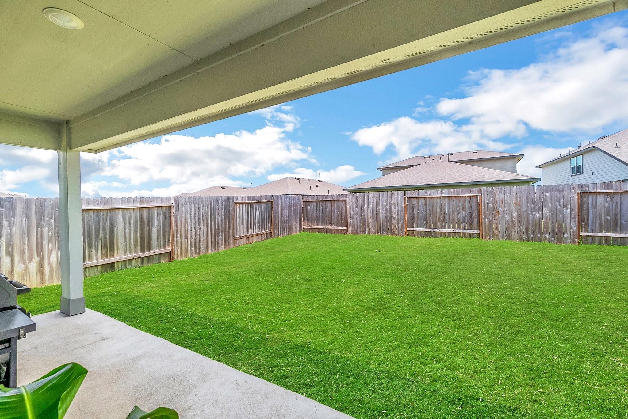 Fenced backyard with a broad lawn, viewed from a covered patio.