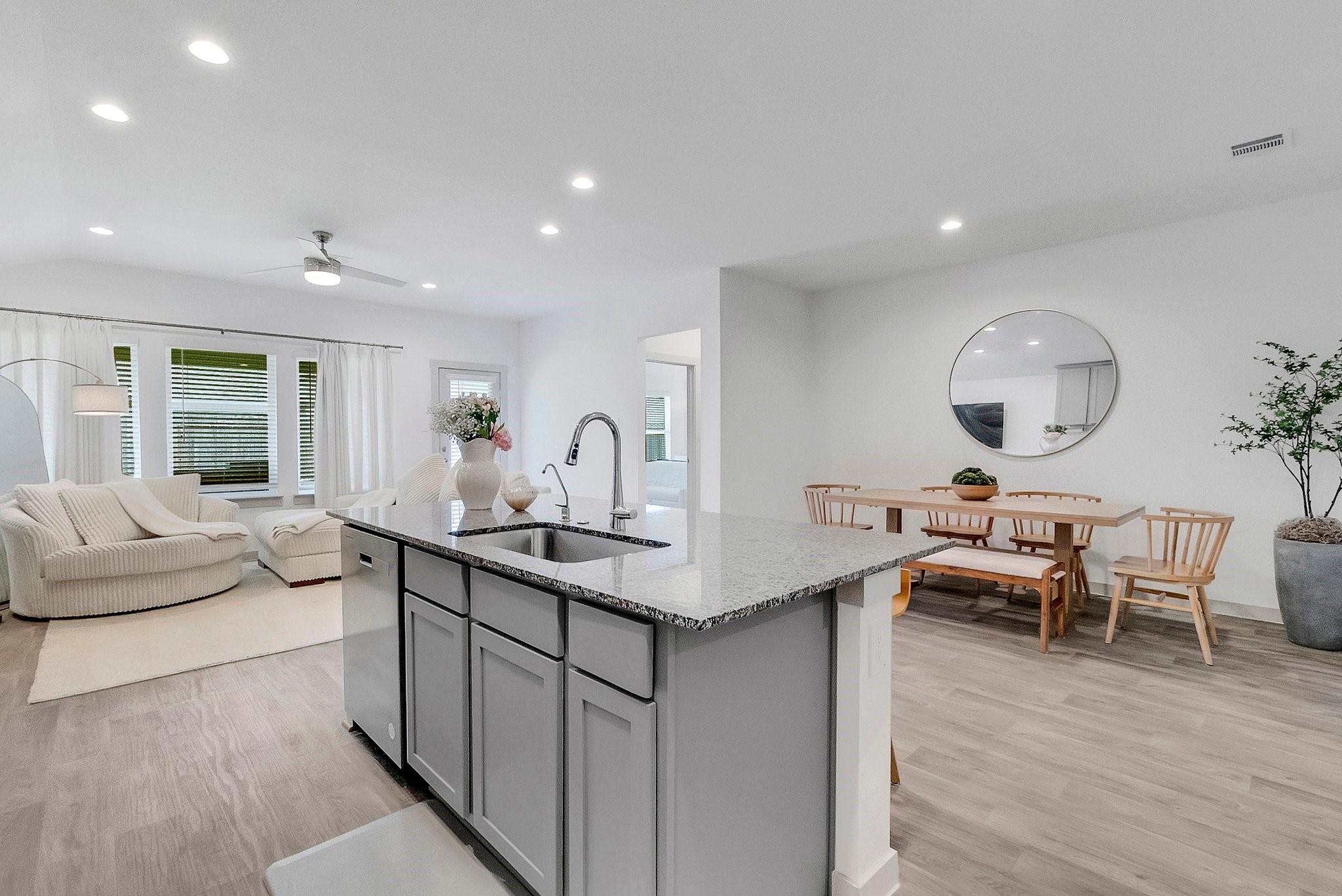 Open-plan kitchen with a granite island, adjoining wood dining table, and cream living room seating.