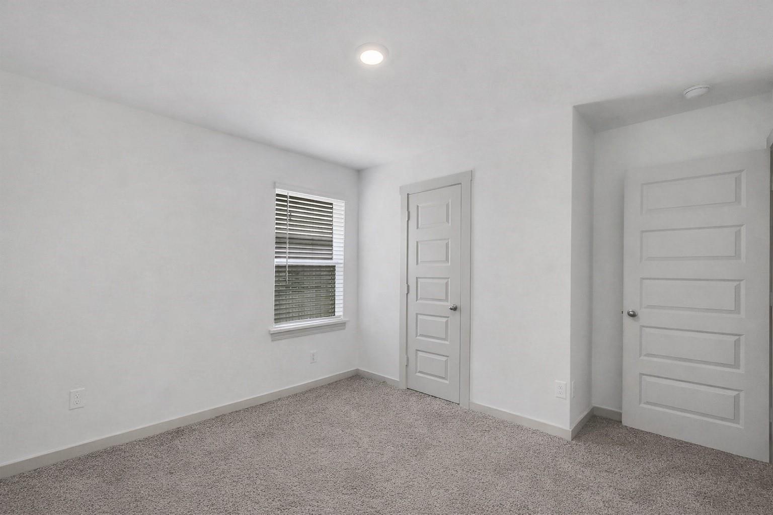 Empty carpeted room with white walls, a window with blinds, and two paneled doors.