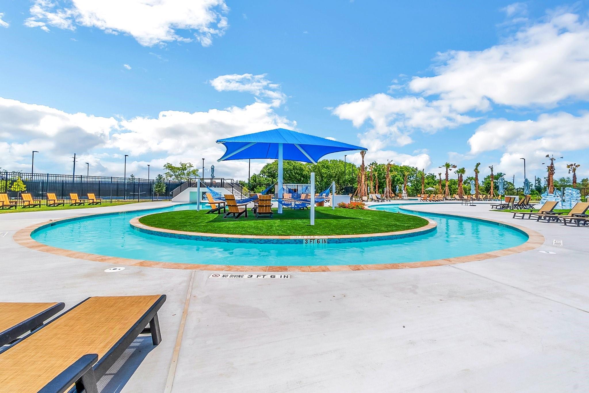 Community pool with a circular shallow section, grassy island, and large blue shade canopy.