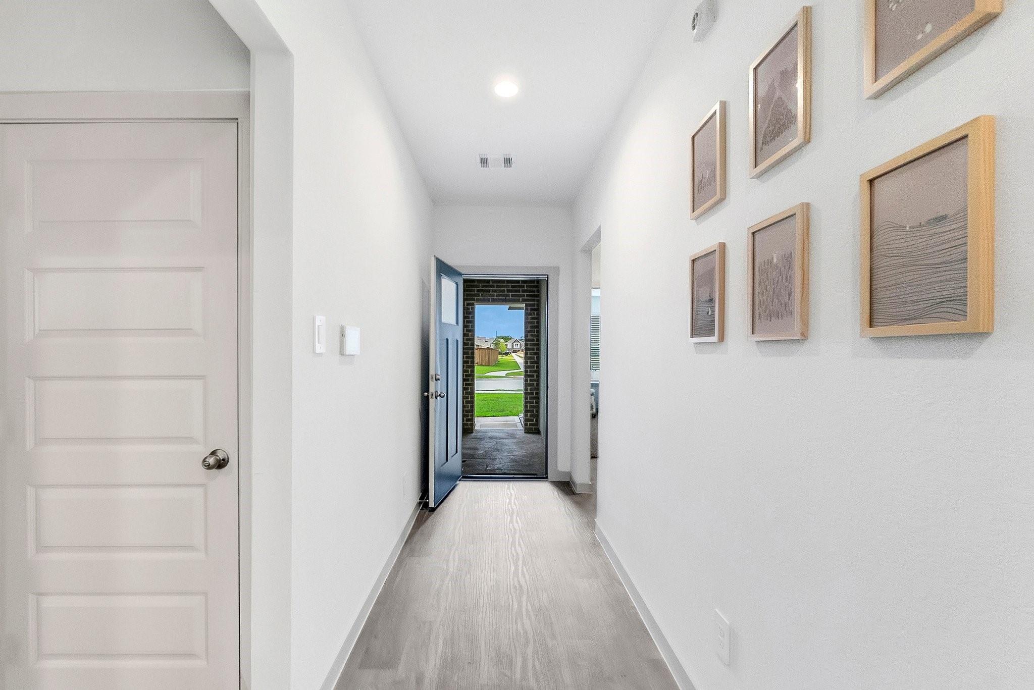 Bright entry hallway with framed wall art and an open blue front door.