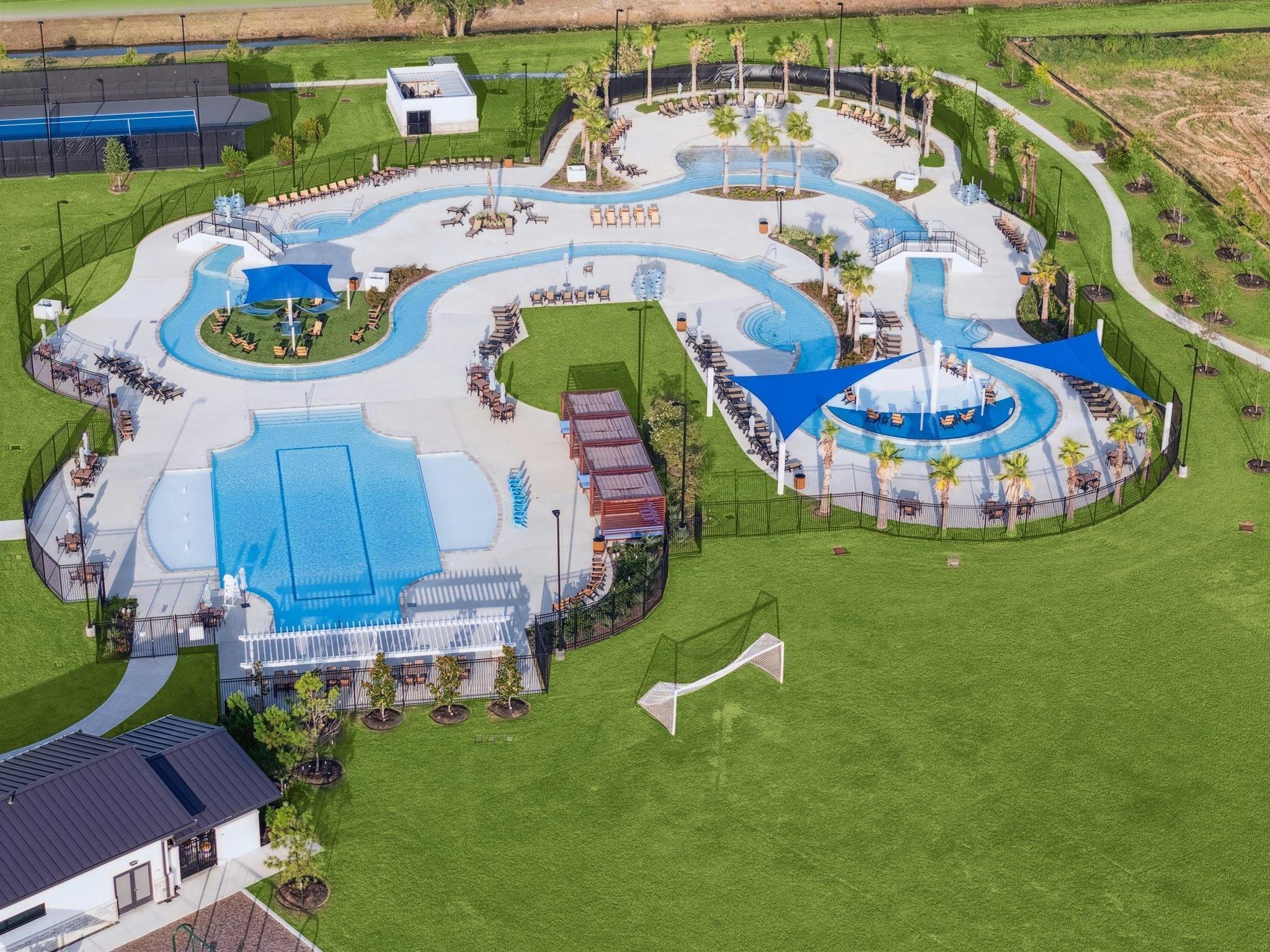 Community pool complex with winding pools, blue shade canopies, and a grassy recreation area.
