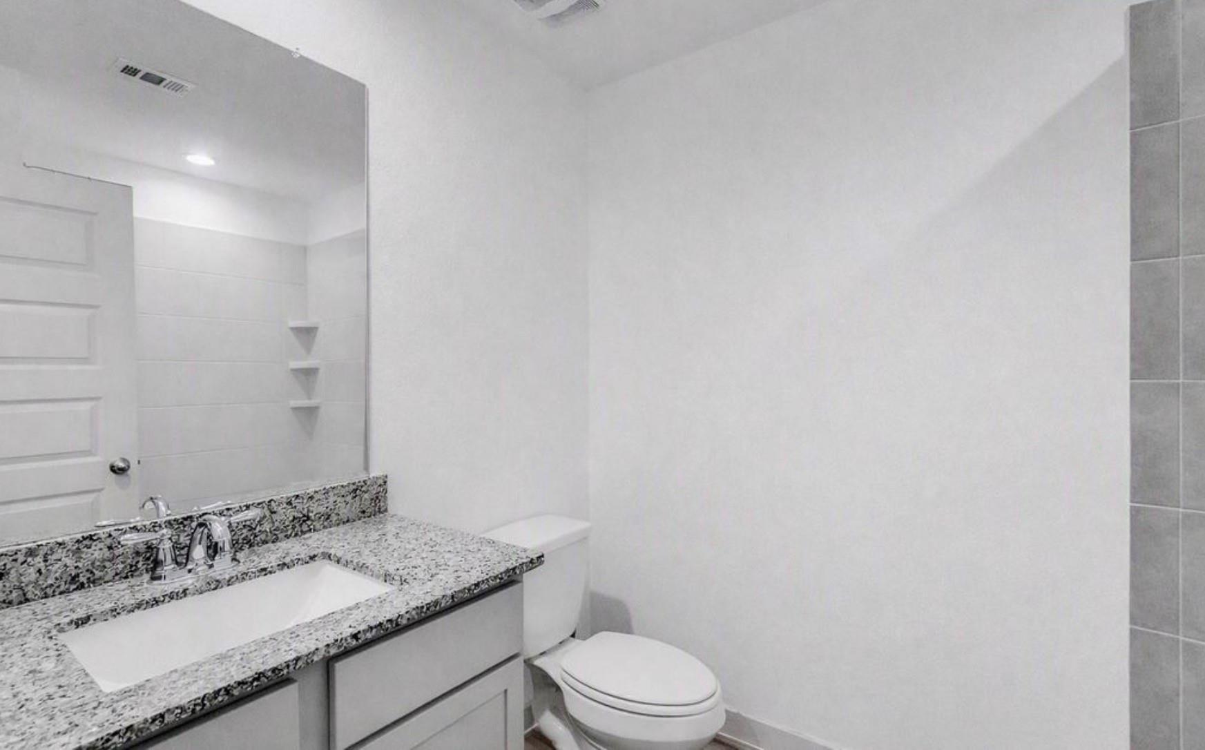 Bathroom with a granite vanity, inset sink, large mirror, and white toilet.