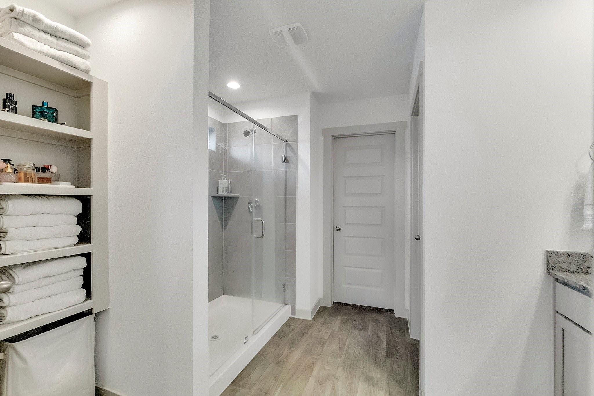 Bathroom with glass shower, built-in towel shelves, and wood-look flooring.