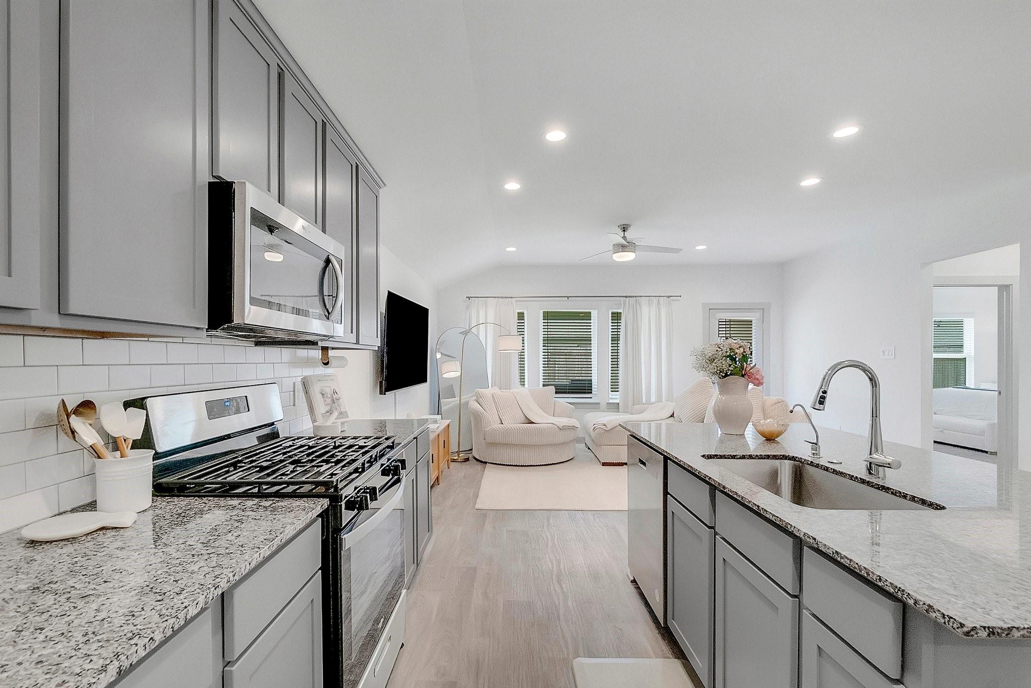 Open-plan kitchen with granite island, stainless steel appliances, and a light-filled living area beyond.
