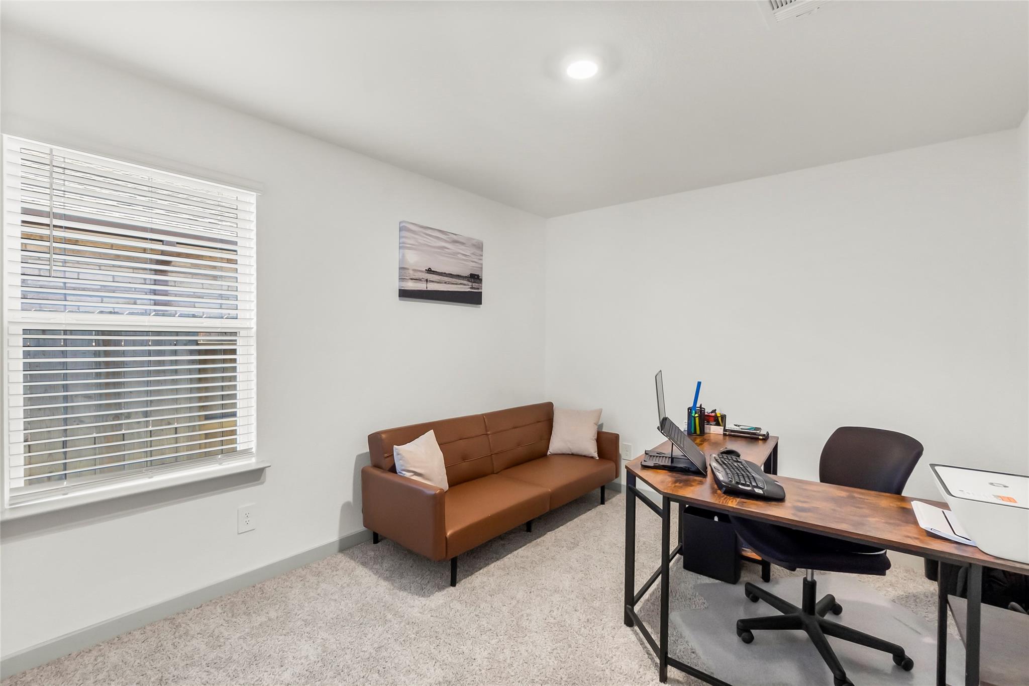 Furnished home office with a wooden desk and computer beside a brown loveseat.