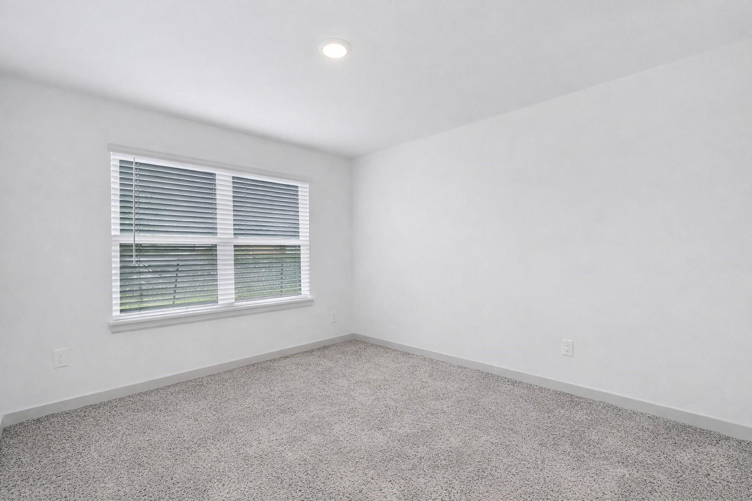 Empty bedroom with gray carpet and a wide window with white blinds.