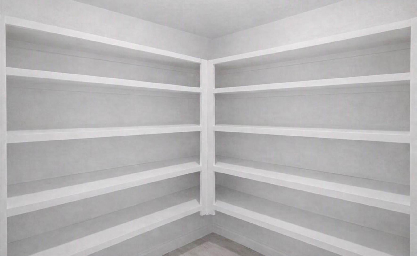 Empty pantry with white built-in shelves wrapping around two walls.