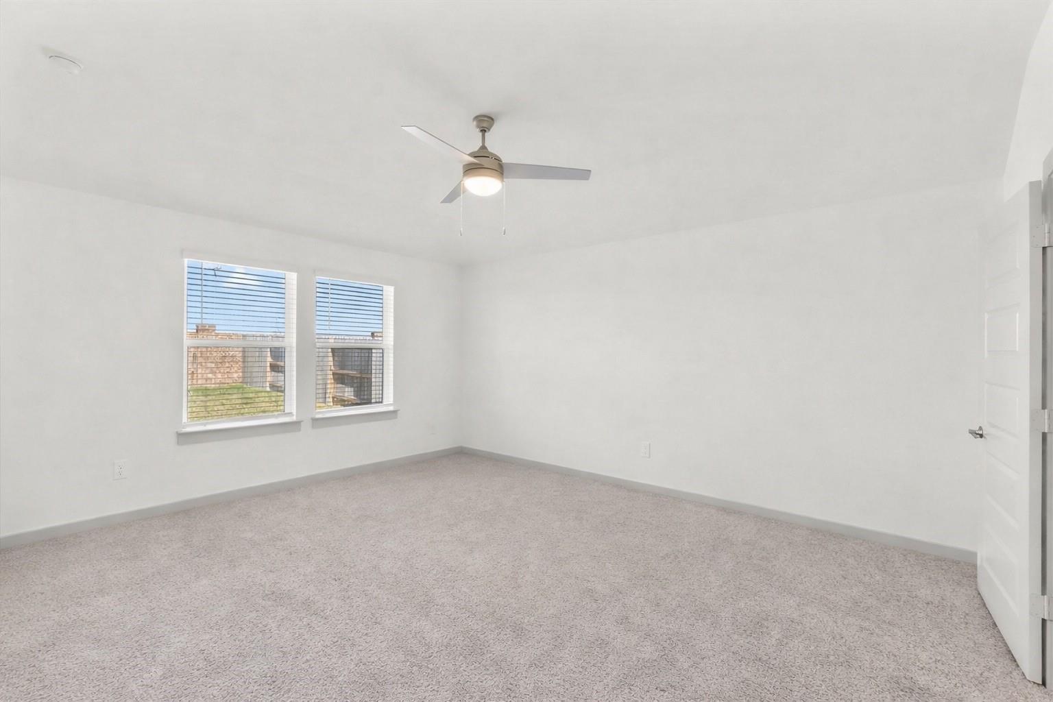 Empty carpeted bedroom with two windows and a ceiling fan.