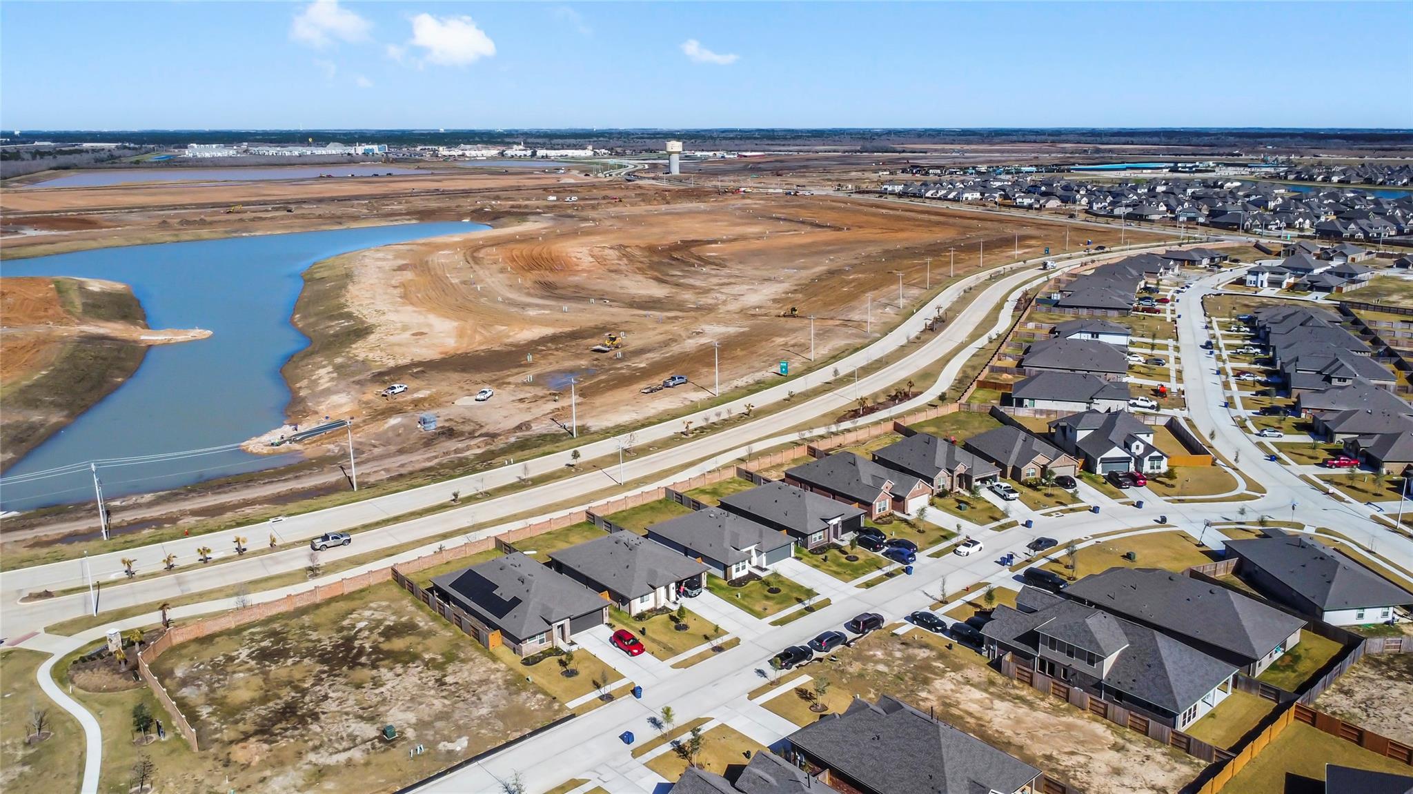 Aerial view of a residential neighborhood beside a graded site and winding waterway.