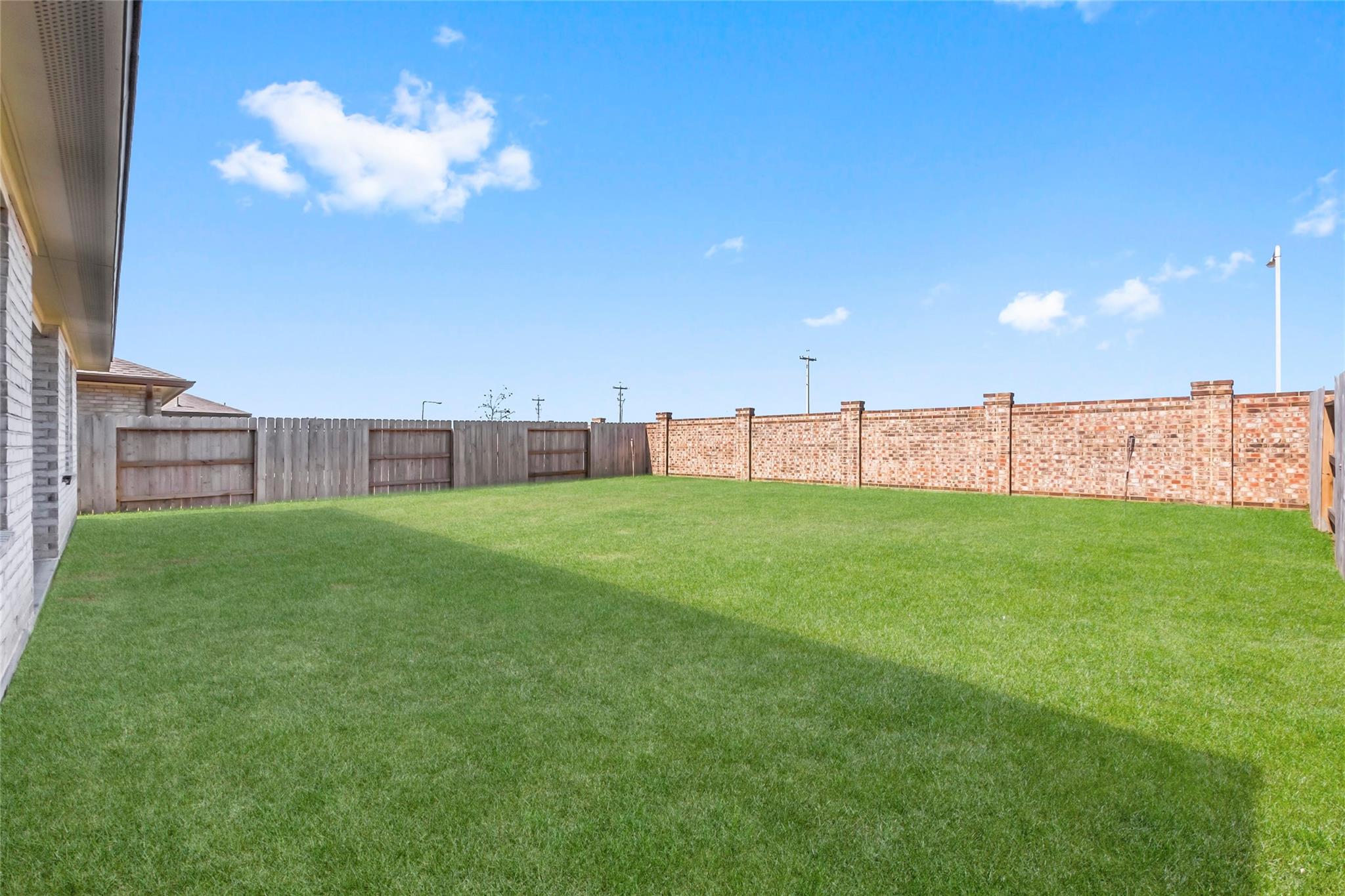 Spacious green backyard with a freshly mown lawn, wooden fencing, and a long brick wall.