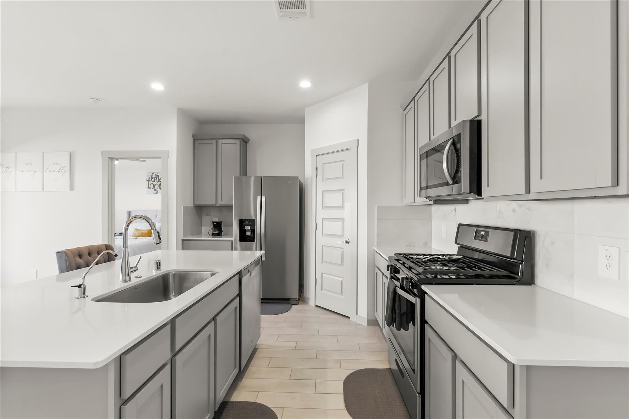 Modern kitchen with gray cabinets, a large white island, and stainless steel appliances.