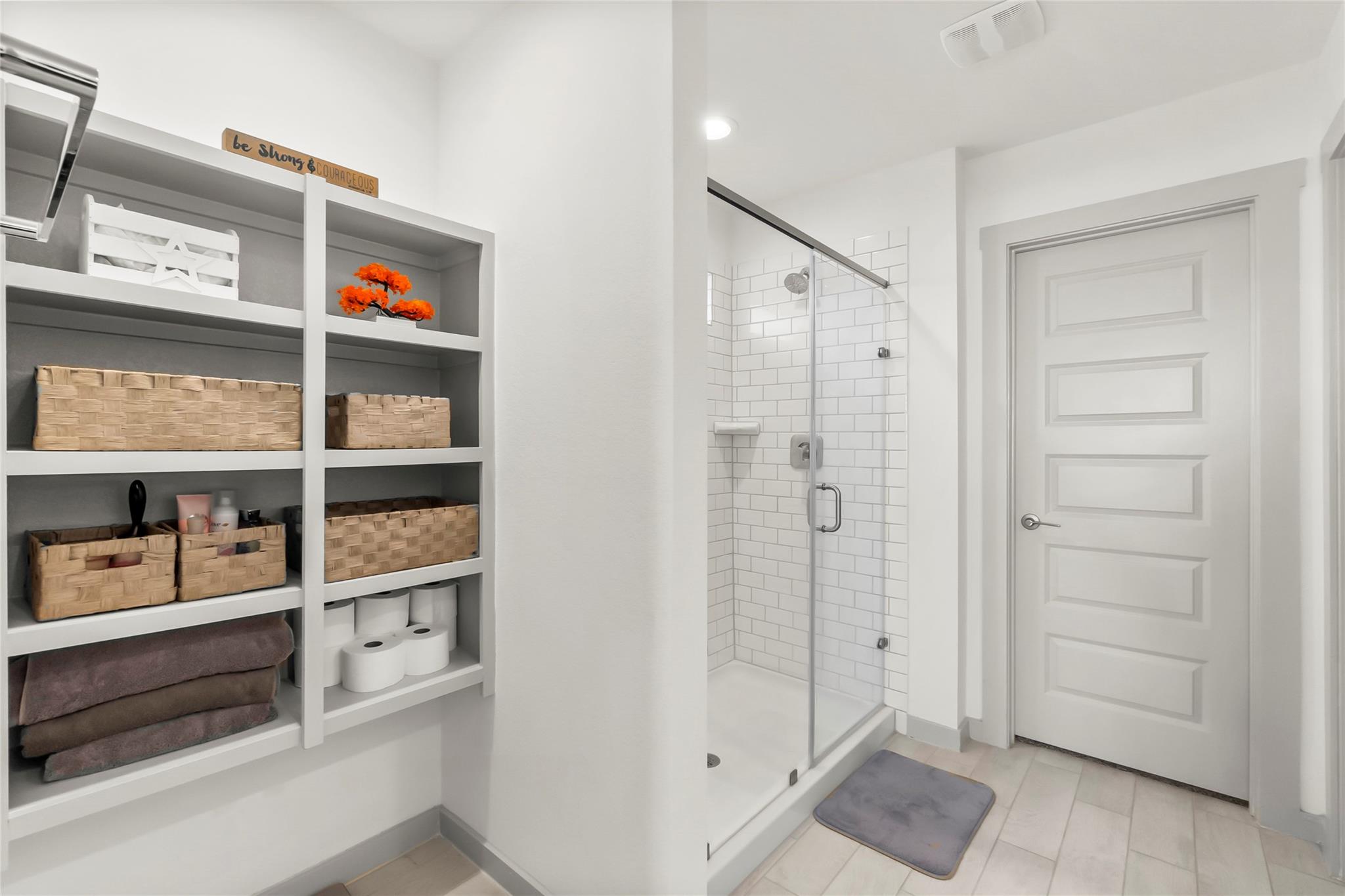 Bathroom with a glass-enclosed subway-tile shower and built-in shelves with woven baskets.