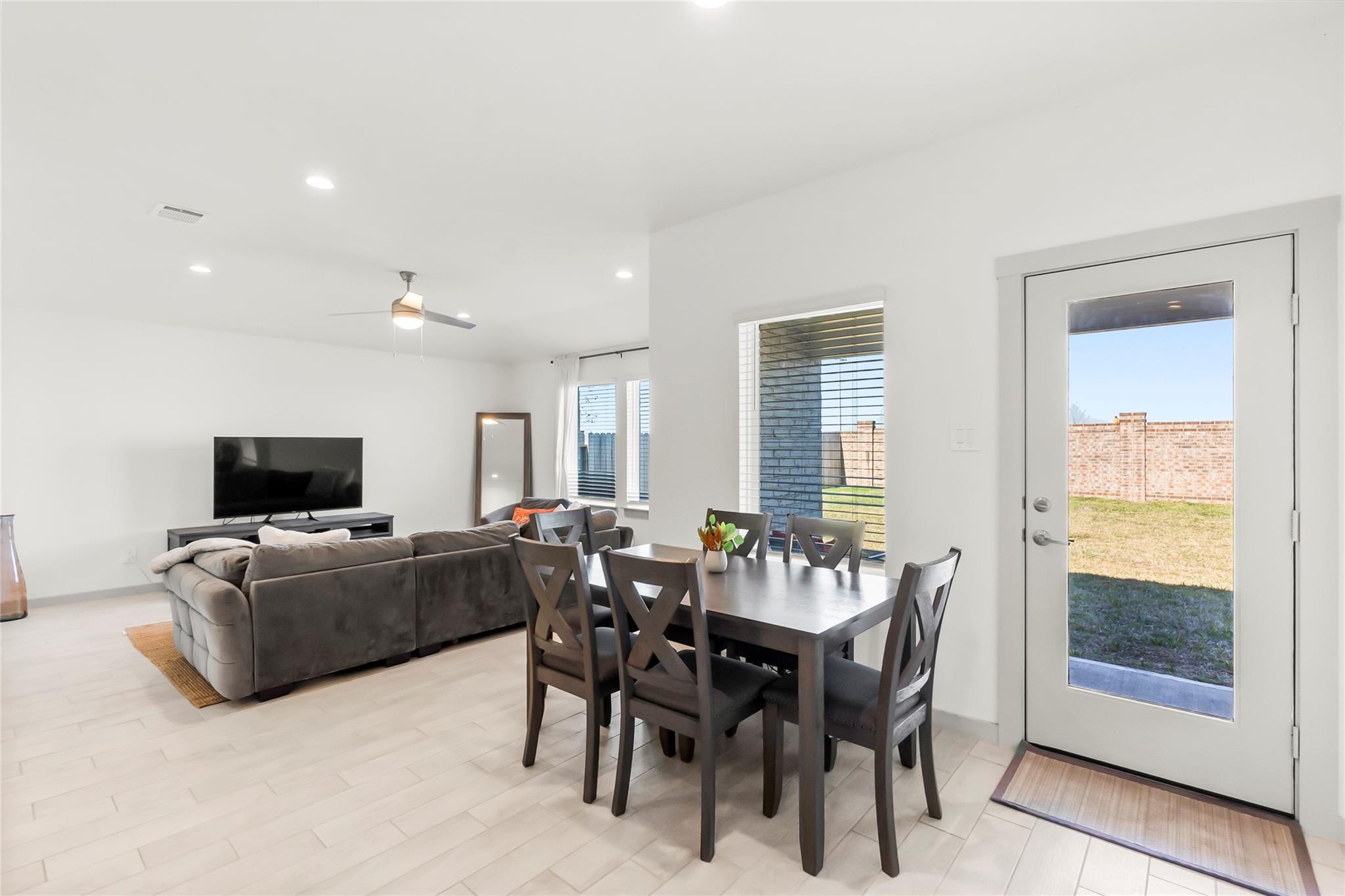 Open-plan living and dining area with a gray sectional, dark wood table, and glass-panel exterior door.