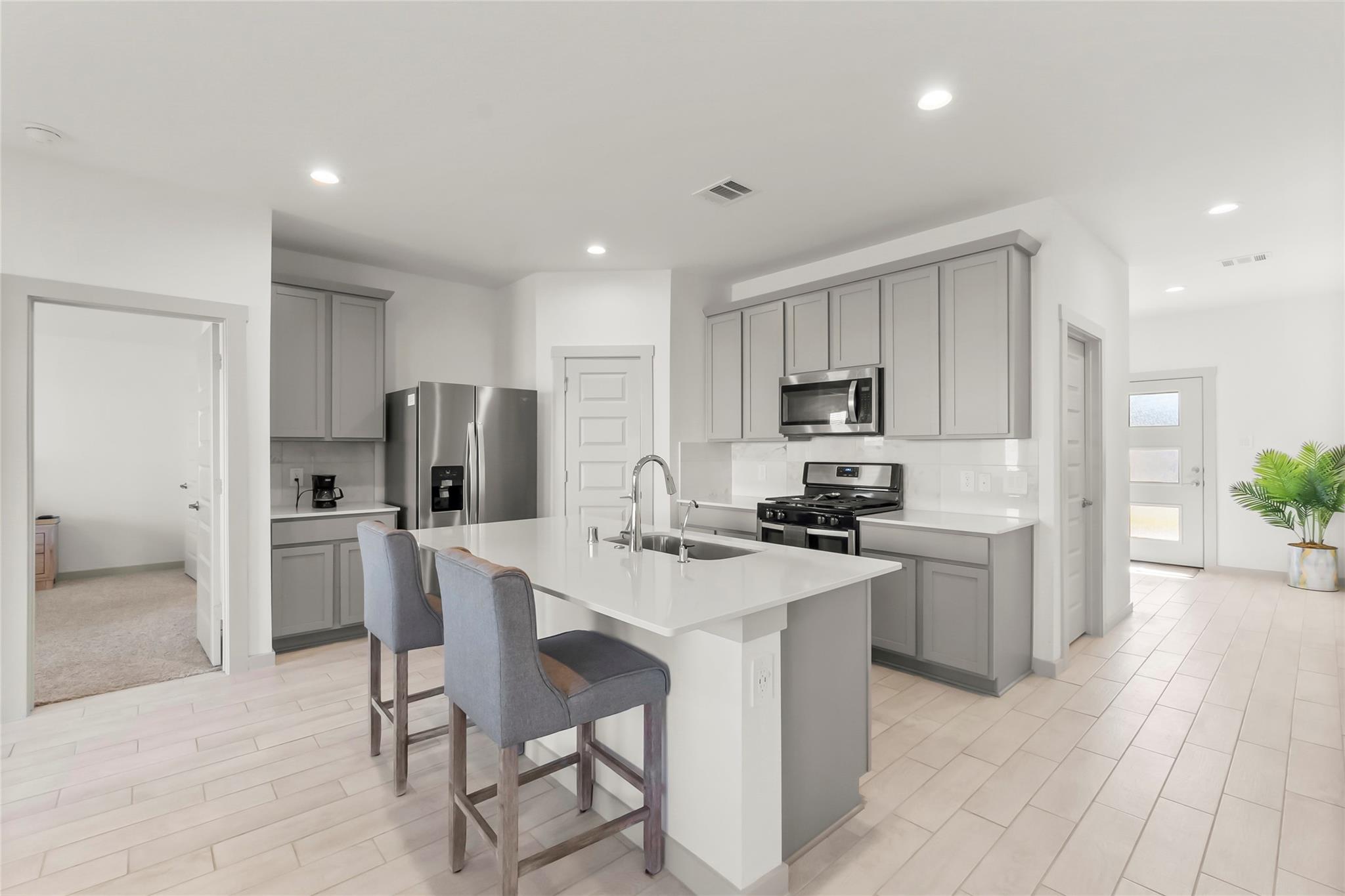 Modern kitchen with gray cabinets, stainless appliances, and a large island with two bar stools.