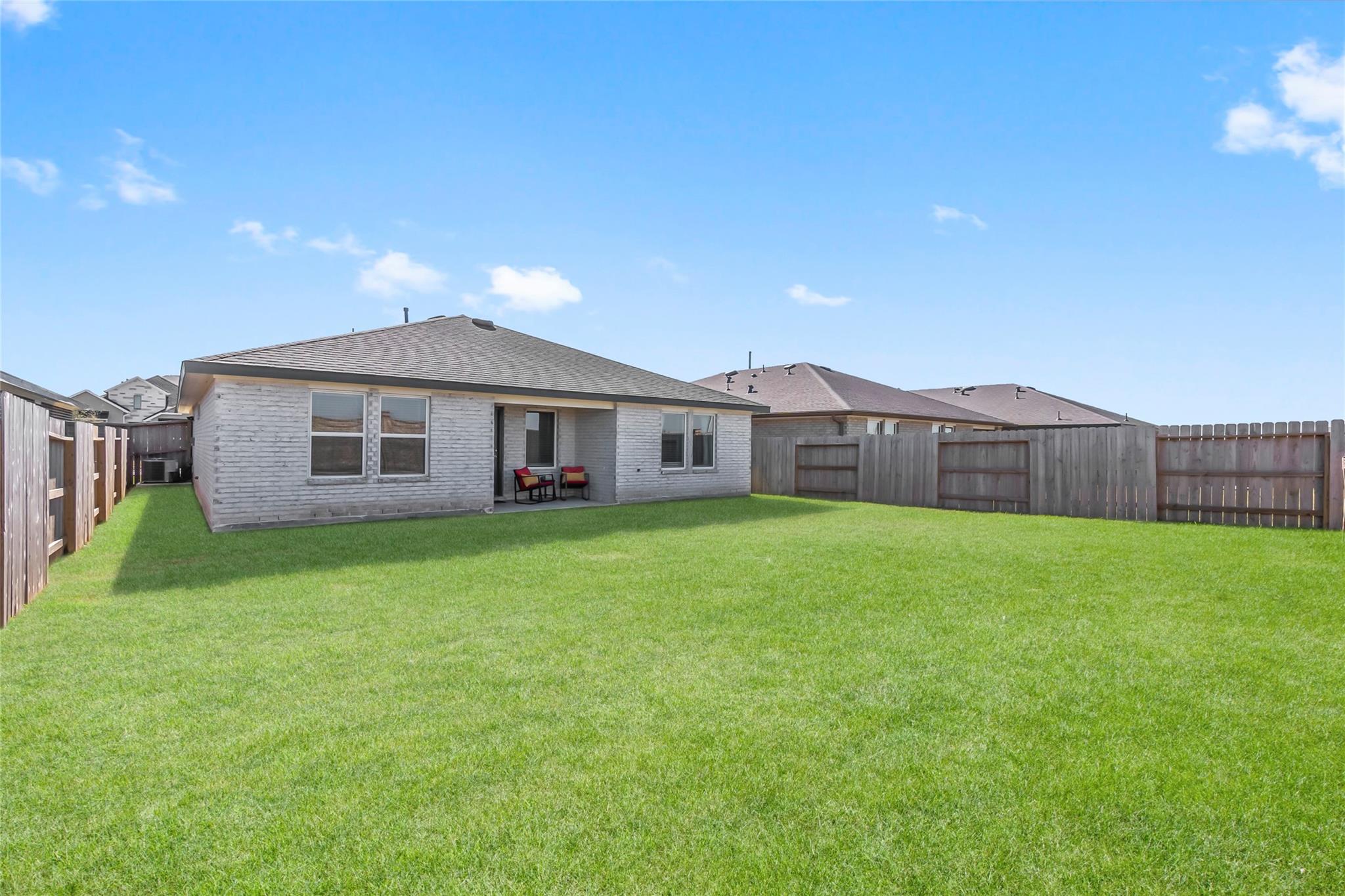 House rear with covered patio and a wide, fenced backyard lawn.