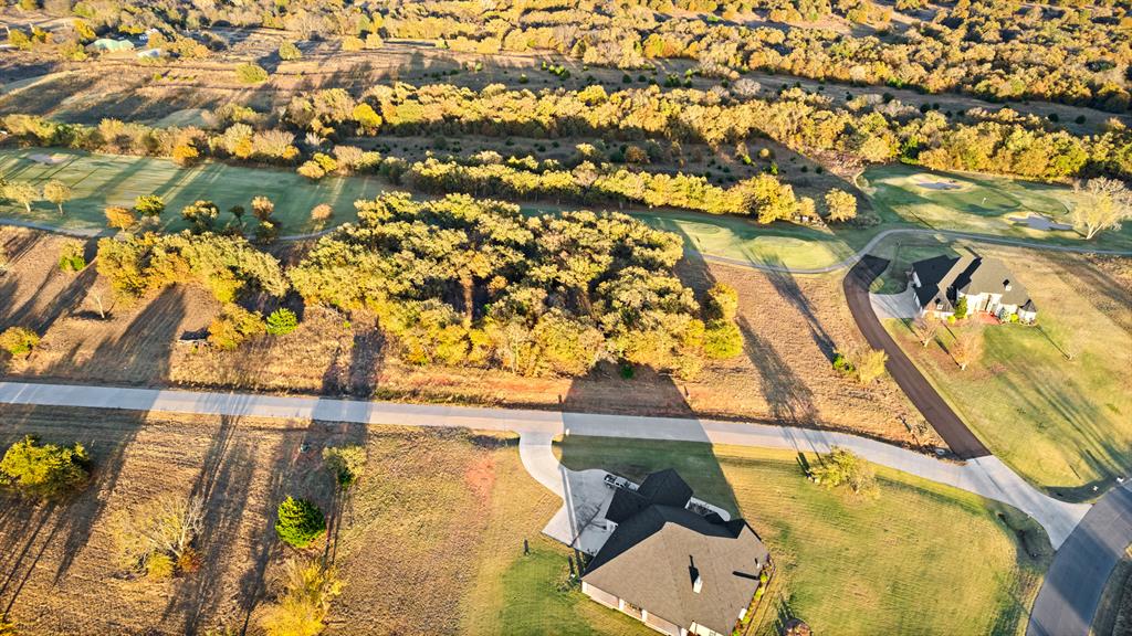 Aerial view of a wooded lot beside a residential road, with nearby homes and autumn trees.