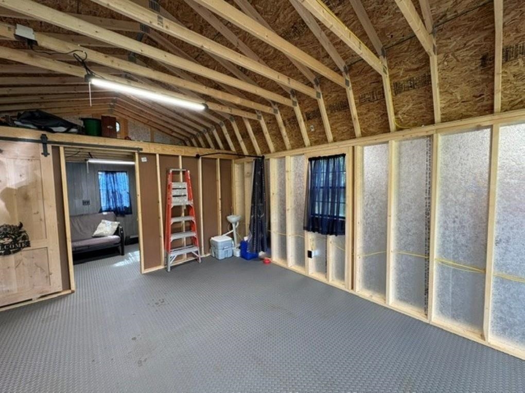 Unfinished interior with exposed rafters, insulated walls, gray carpet, and a ladder by an open doorway.