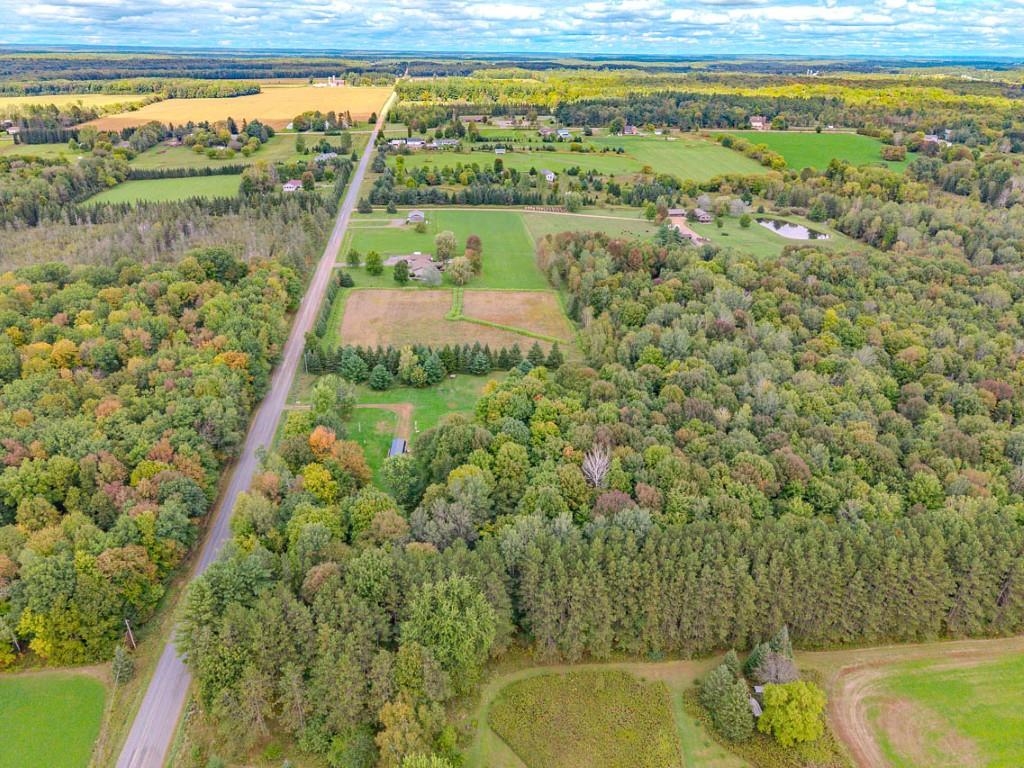 Aerial view of wooded rural acreage, open fields, and a road through the autumn landscape.