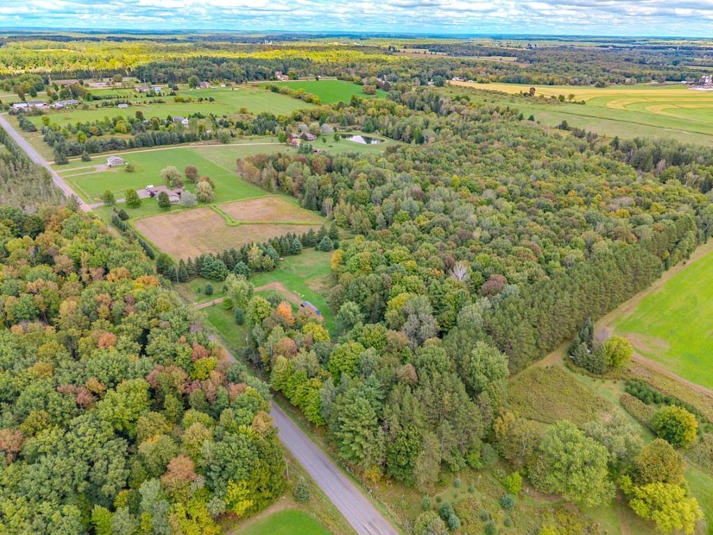 Aerial view of wooded rural acreage, open fields, and scattered homes along a winding road.