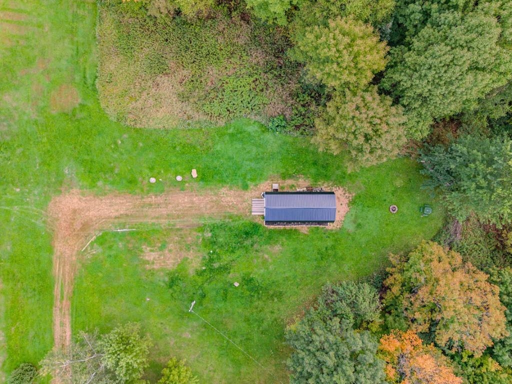 Aerial view of a grassy, tree-lined property with a long metal-roofed building and dirt driveway.