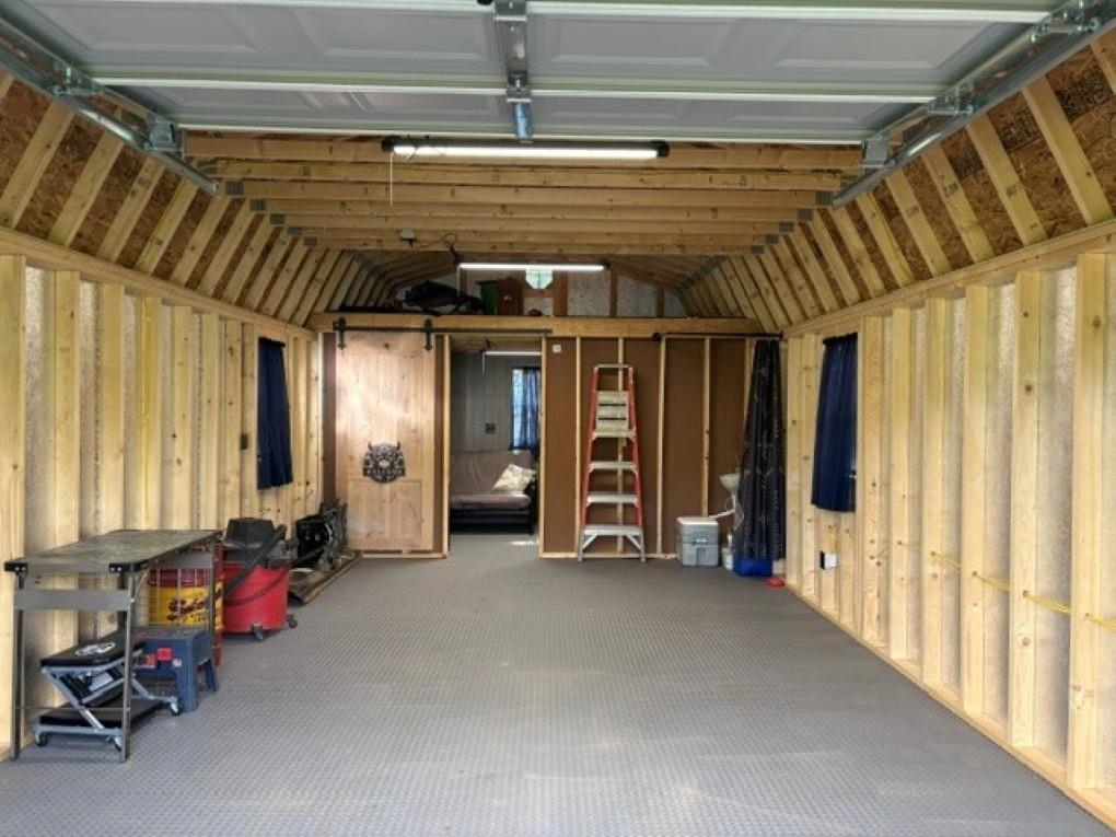 Garage interior with exposed wood framing, a raised overhead door, workbench, and storage.