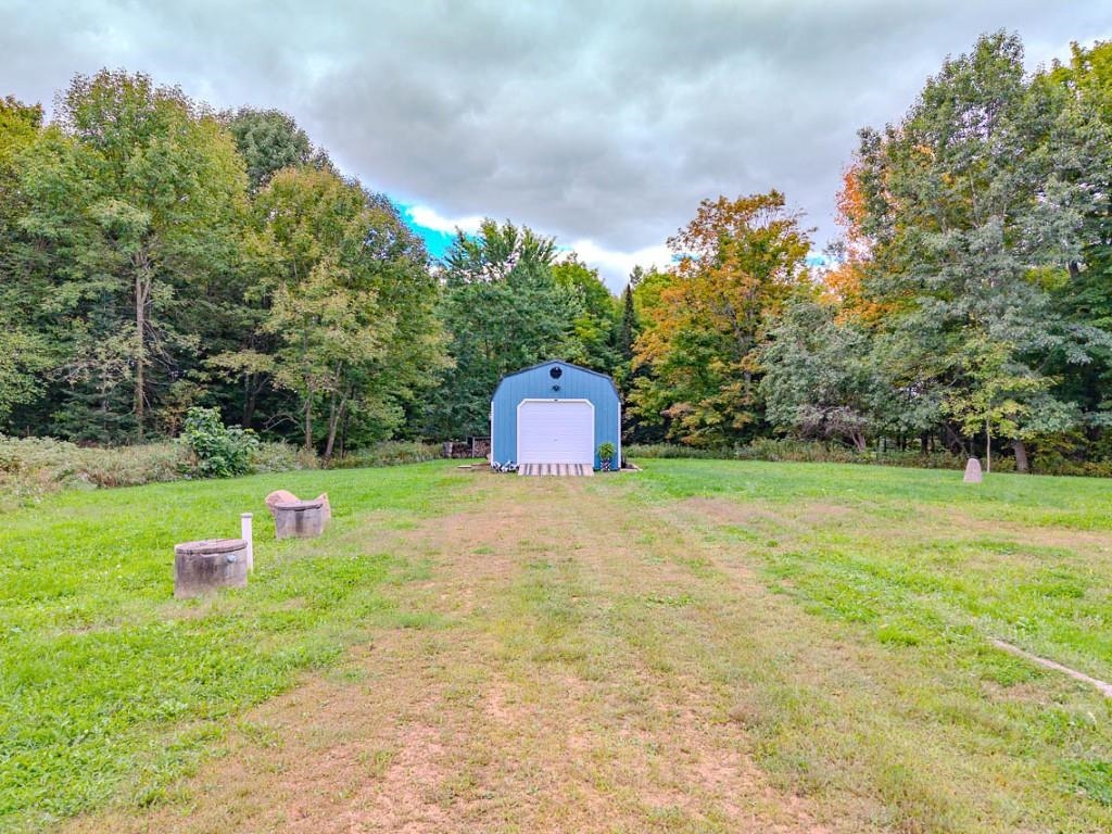 Blue storage shed with a white roll-up door at the edge of a grassy, tree-lined yard.