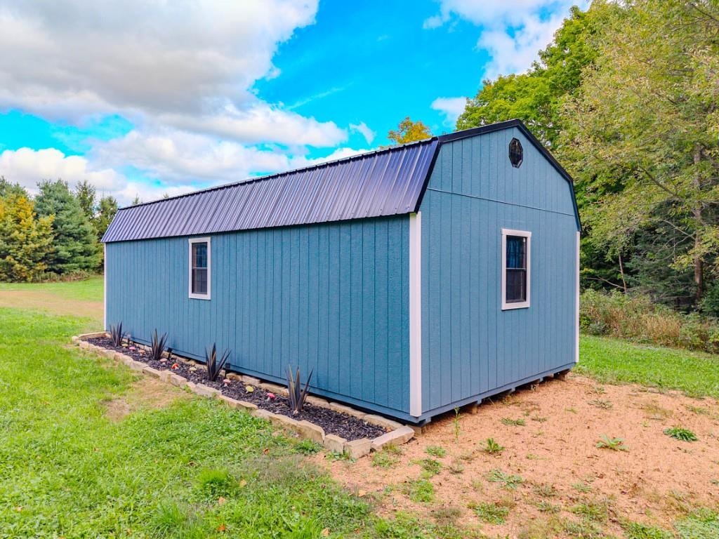 Blue detached storage shed with a dark metal roof and two windows on a grassy lot.
