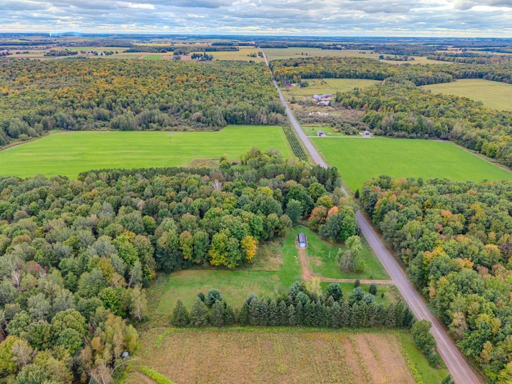 Aerial view of wooded acreage and green fields beside a rural road.