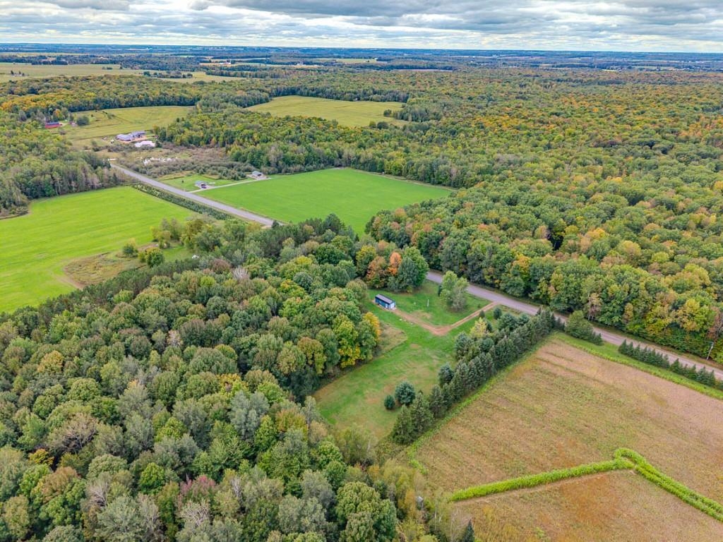 Aerial view of wooded rural acreage, surrounding fields, and a small outbuilding.