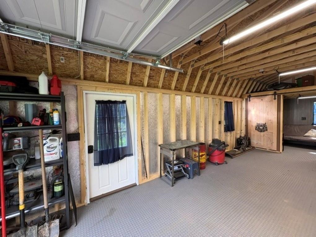 Garage with exposed wood framing, storage shelves, tools, and a white door with a blue curtain.
