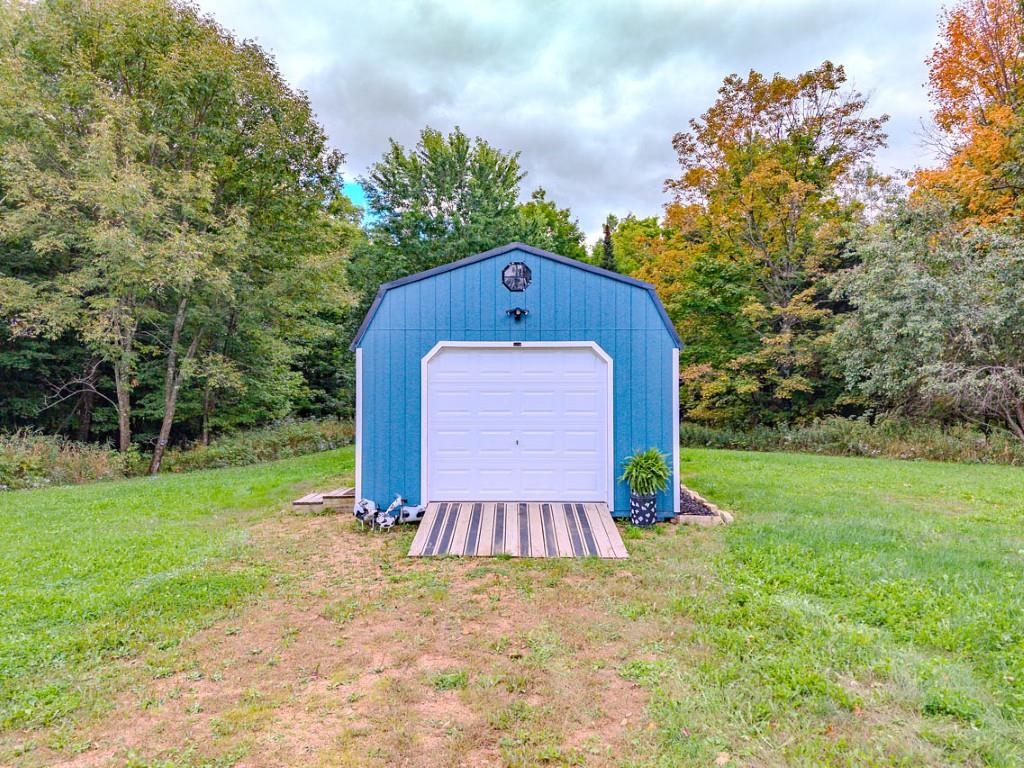Blue detached garage with a white overhead door and striped wooden ramp, surrounded by autumn trees.