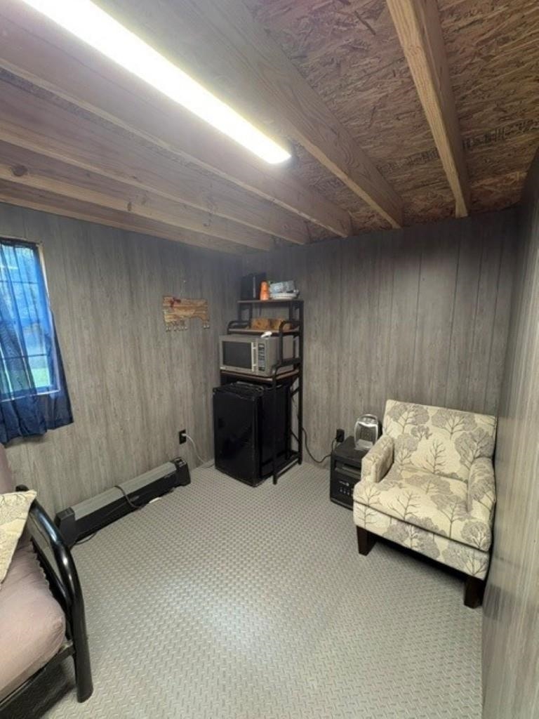 Furnished room with an exposed wood ceiling, patterned armchair, and microwave atop a mini fridge.