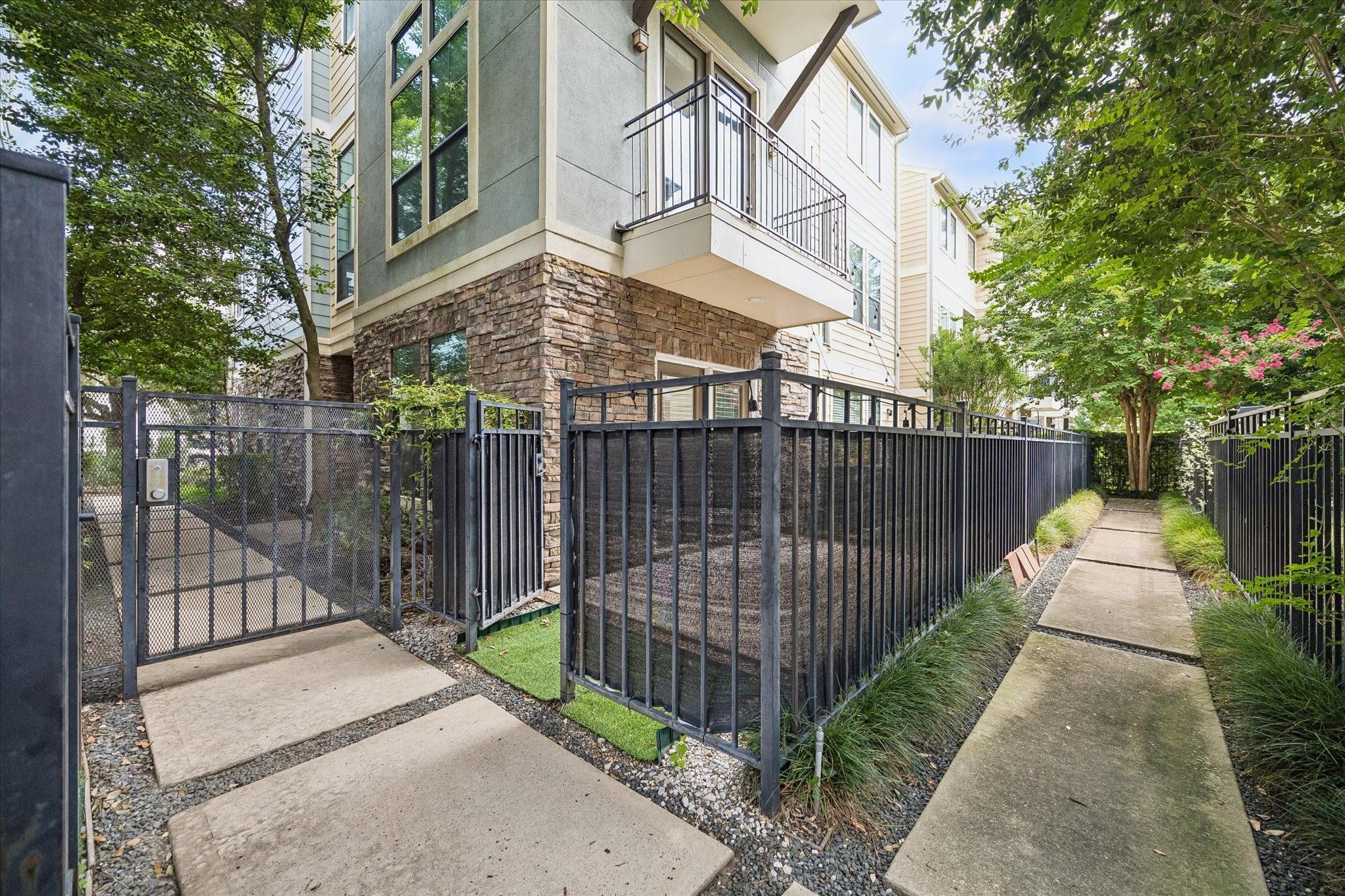 Home exterior with a stone facade, fenced patio, upper balcony, and landscaped walkway.