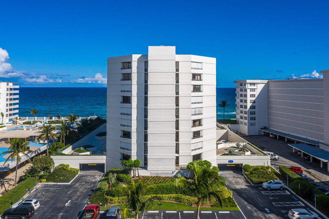 White oceanfront condominium tower with the ocean and neighboring buildings behind it.