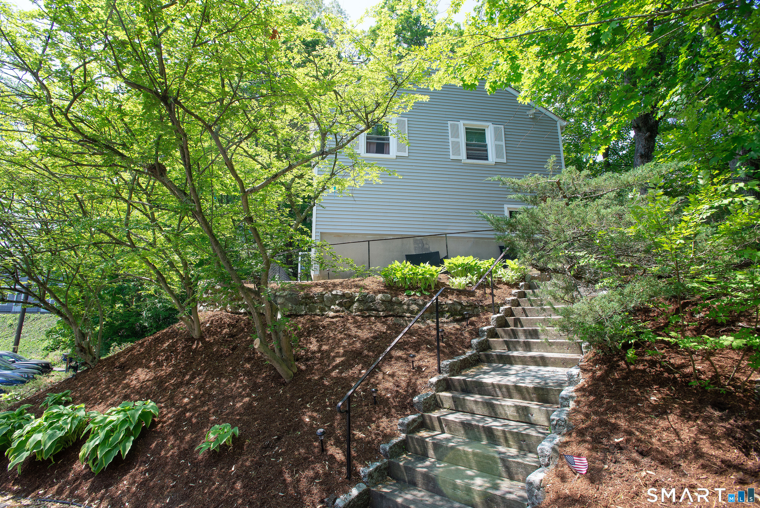 Gray-sided house above a stone-edged staircase, surrounded by mature trees and landscaped grounds.