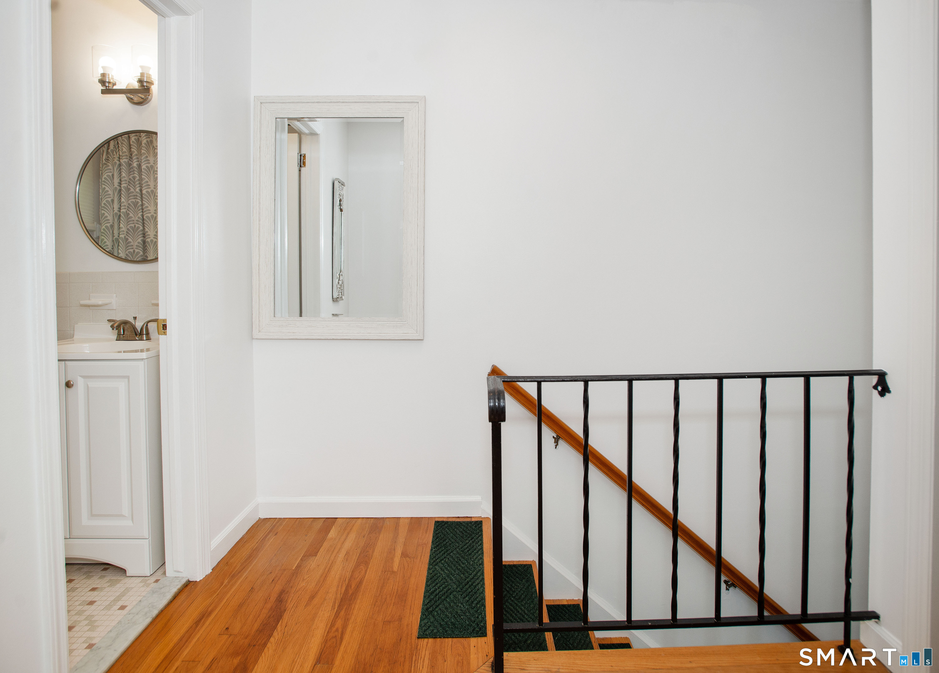 Hallway landing with hardwood floors, black stair railing, and a bathroom vanity visible through the doorway.