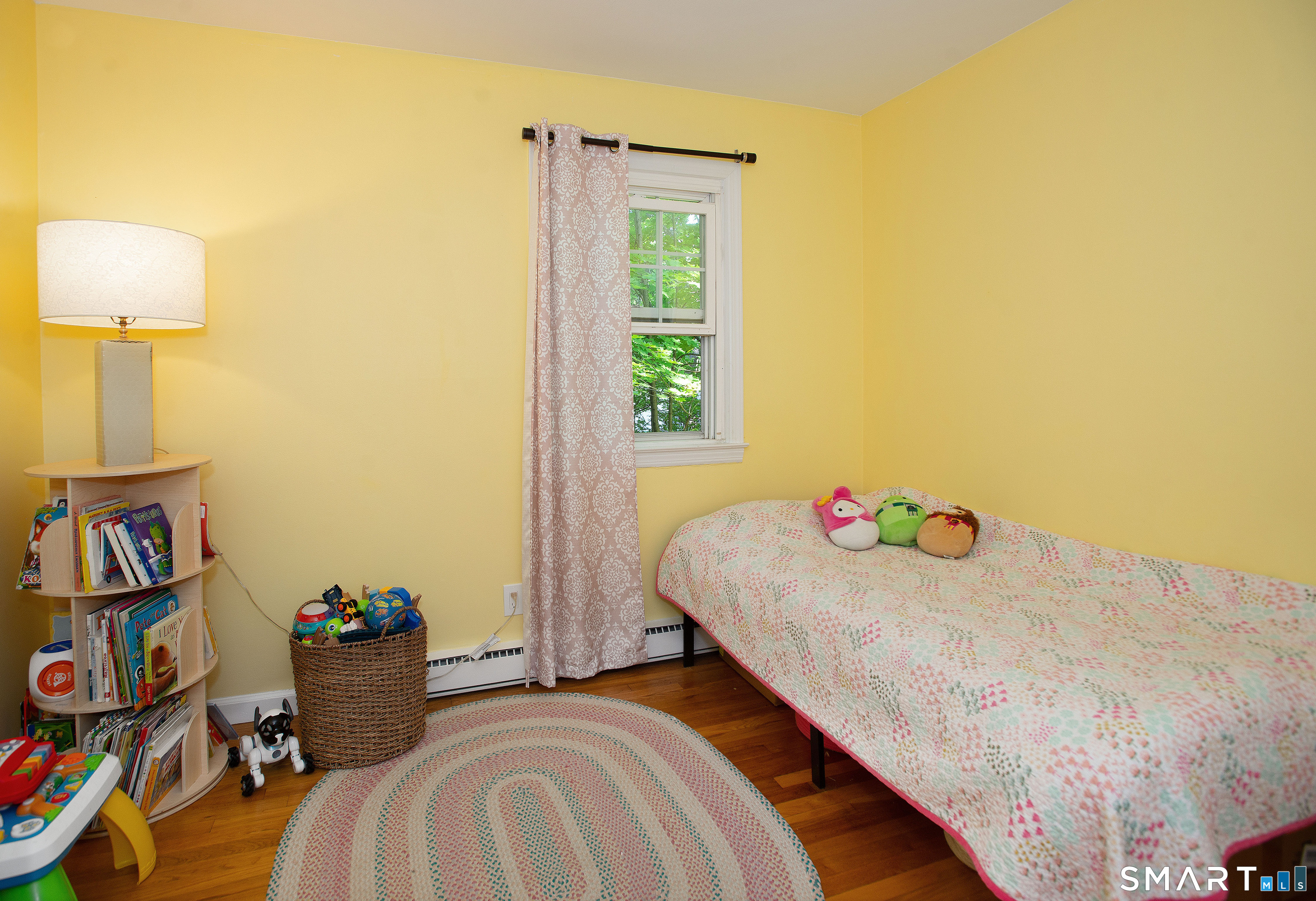 Bedroom with a floral-quilted bed, yellow walls, and shelves of books and toys.