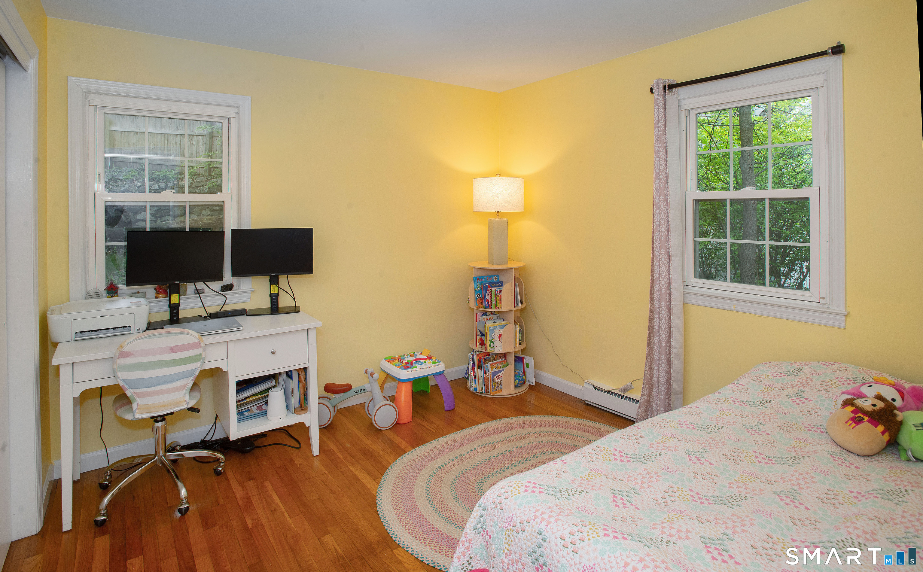 Bedroom with yellow walls, hardwood floors, floral bedding, and a desk beneath the window.