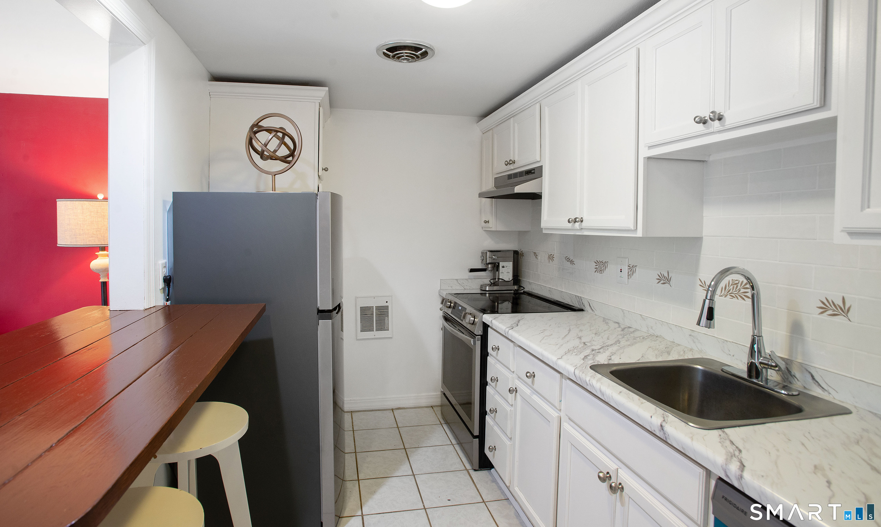 Compact kitchen with white cabinets, marble-look counters, stainless appliances, and a wooden breakfast bar.