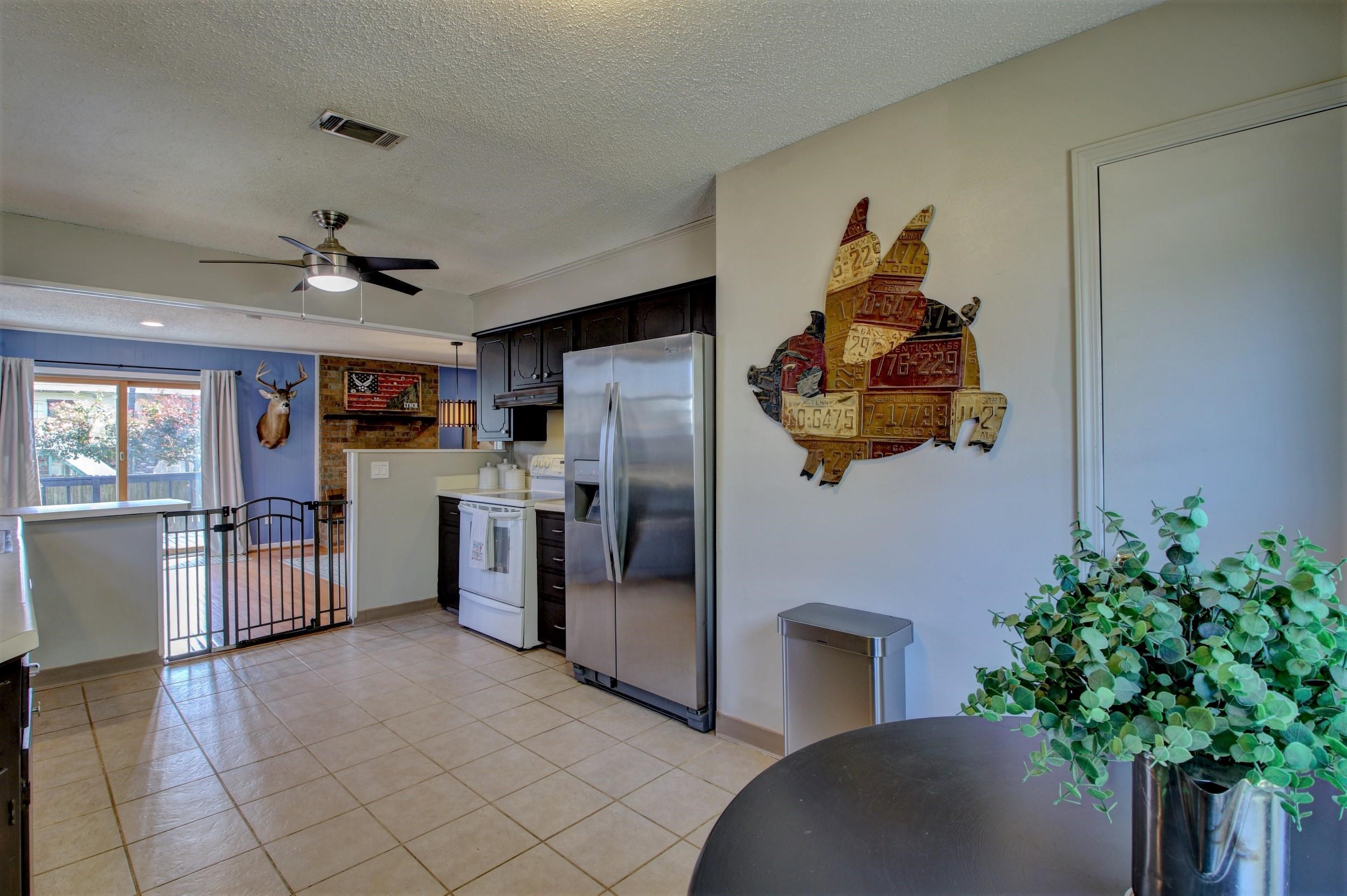 Kitchen with dark cabinets, stainless steel refrigerator, tiled floor, and a gated opening to the dining area.