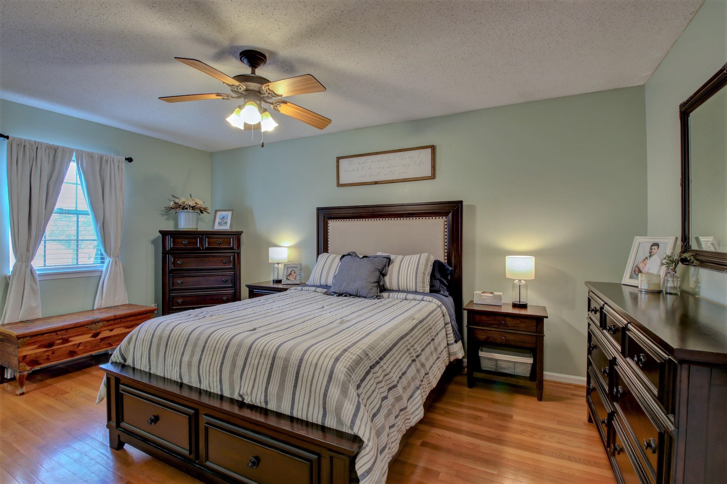 Bedroom with striped bedding, dark wood furniture, a ceiling fan, and warm hardwood floors.