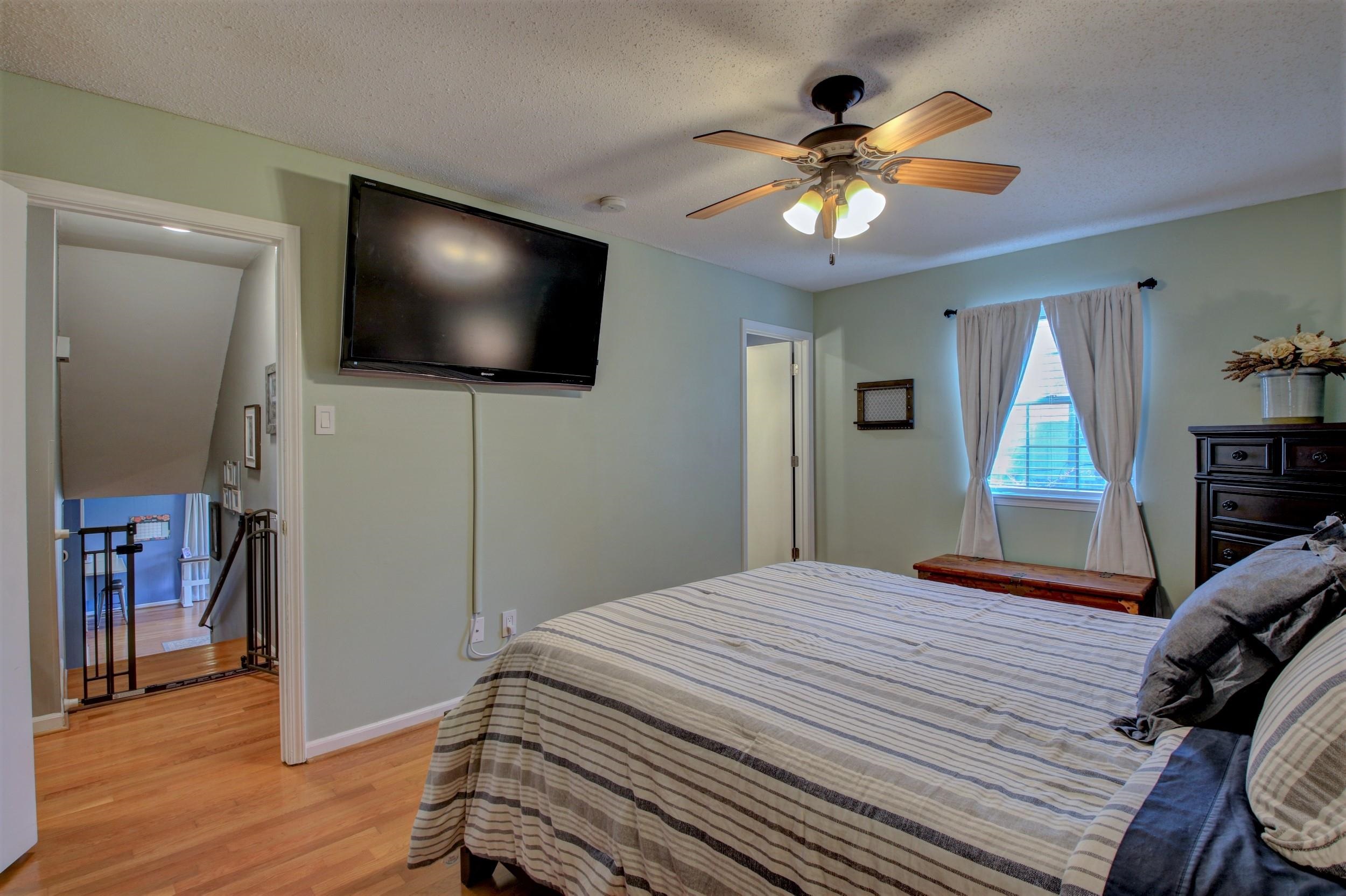 Furnished bedroom with a striped bedspread, wall-mounted television, and ceiling fan.