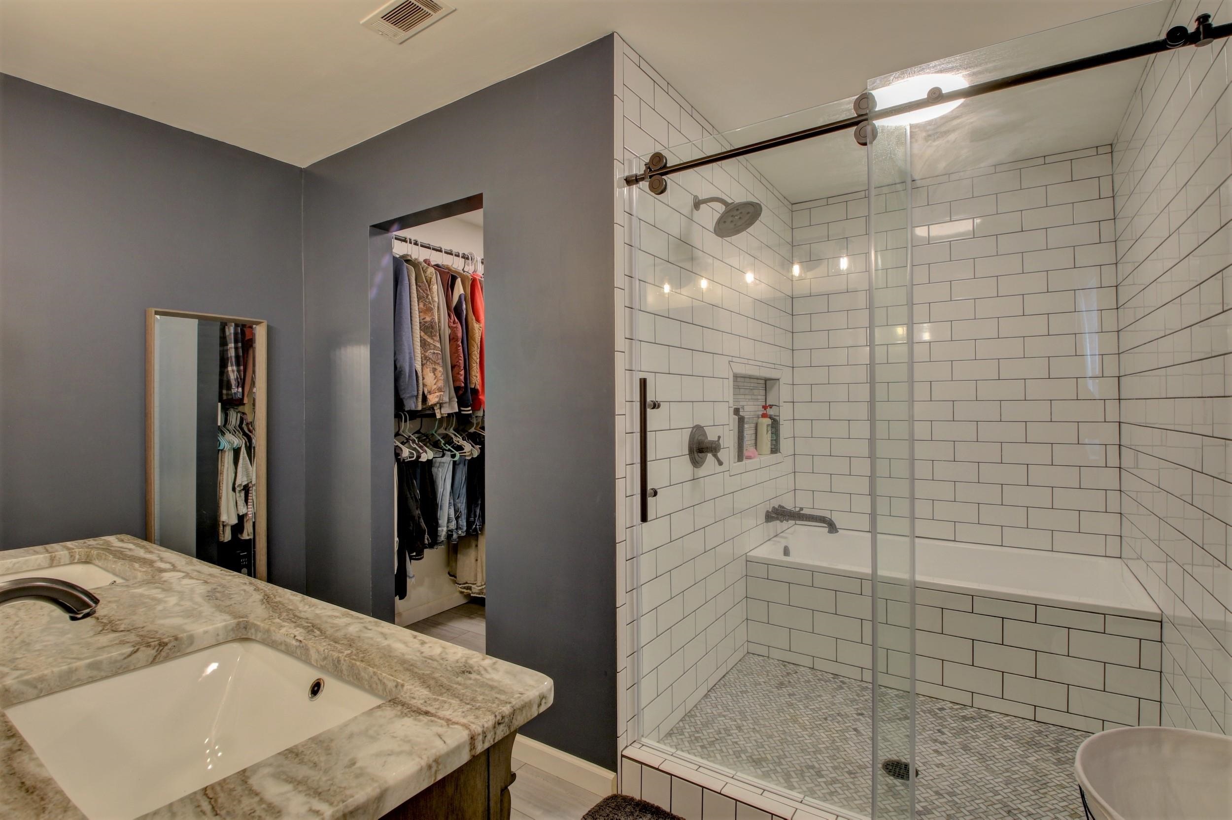 Bathroom with a glass-enclosed subway-tile shower, mosaic floor, and marble-look vanity beside an open closet.