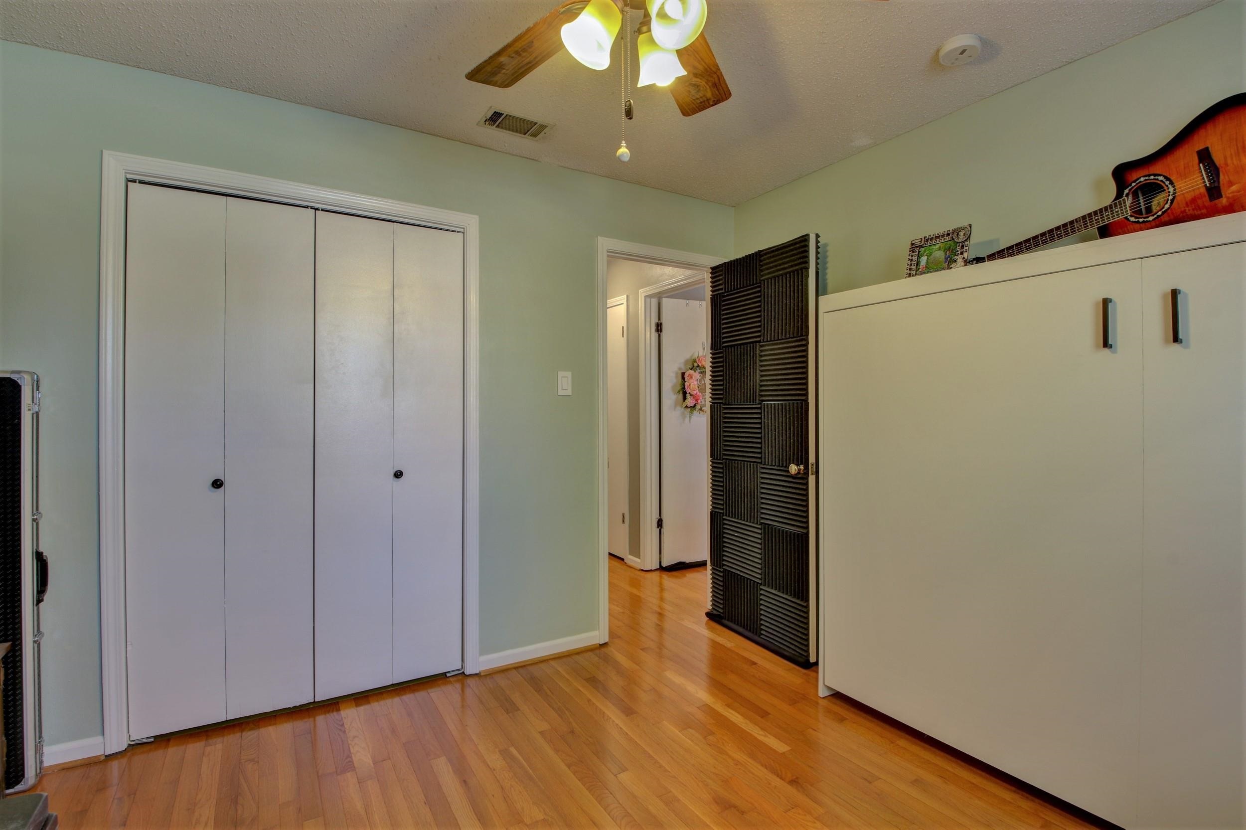Bedroom with hardwood floors, white wardrobes, and a ceiling fan; a guitar hangs above a large cabinet.