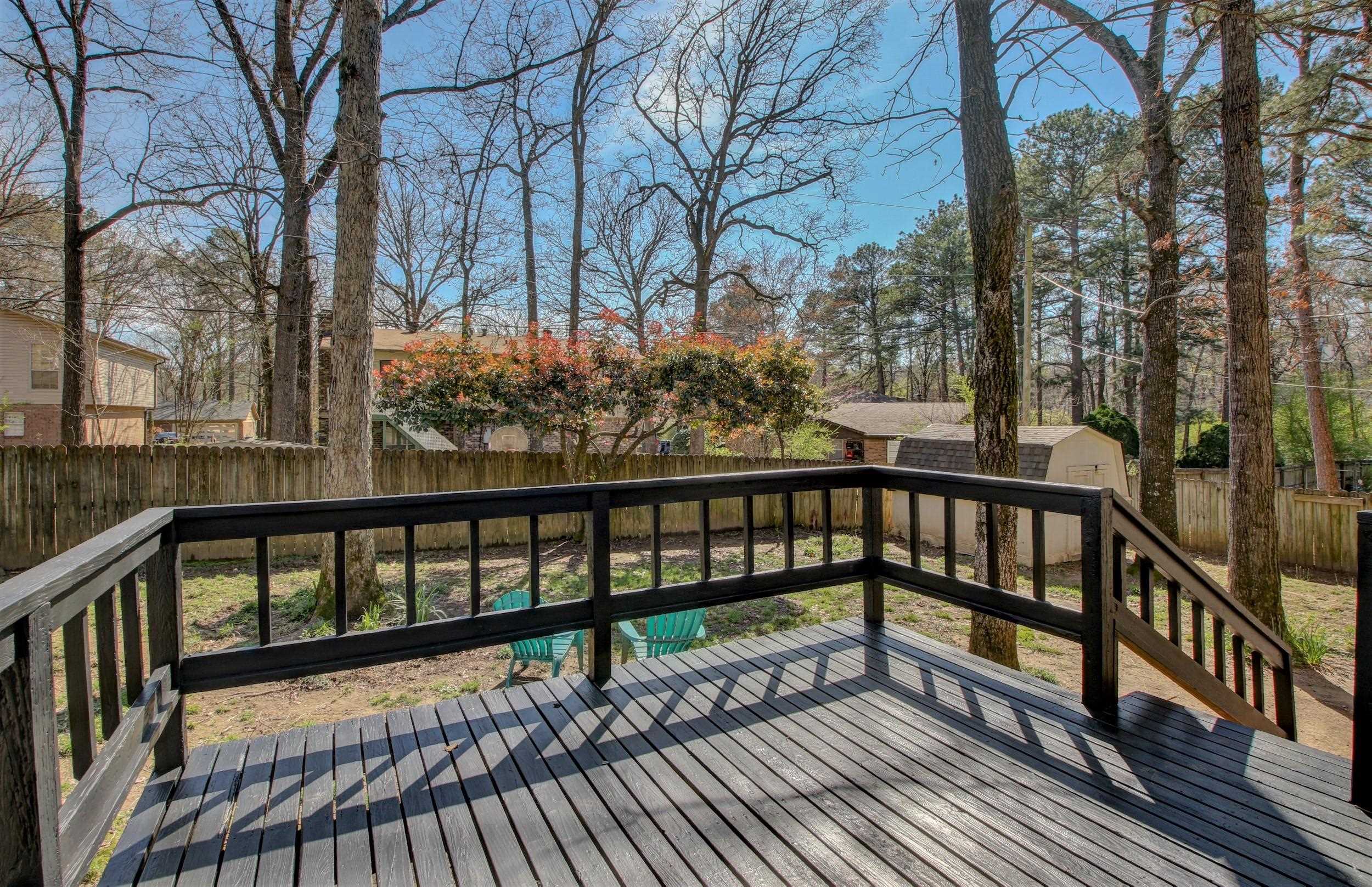 Backyard deck with black railings and turquoise chairs overlooking a fenced, tree-filled yard.