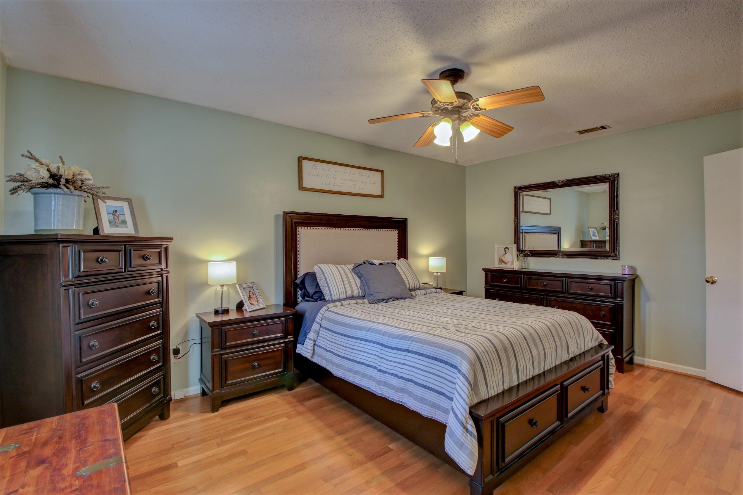 Bedroom with striped bedding, dark wood furniture, hardwood floors, and a ceiling fan.