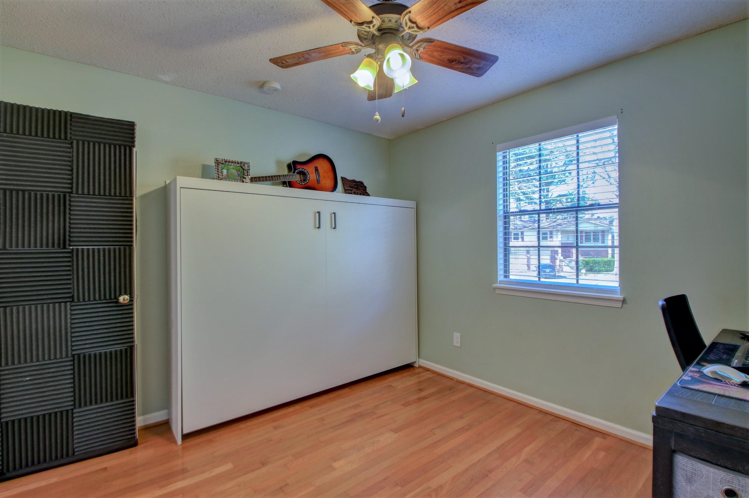 Room with a fold-down bed cabinet, acoustic panels, and guitar beside a window.