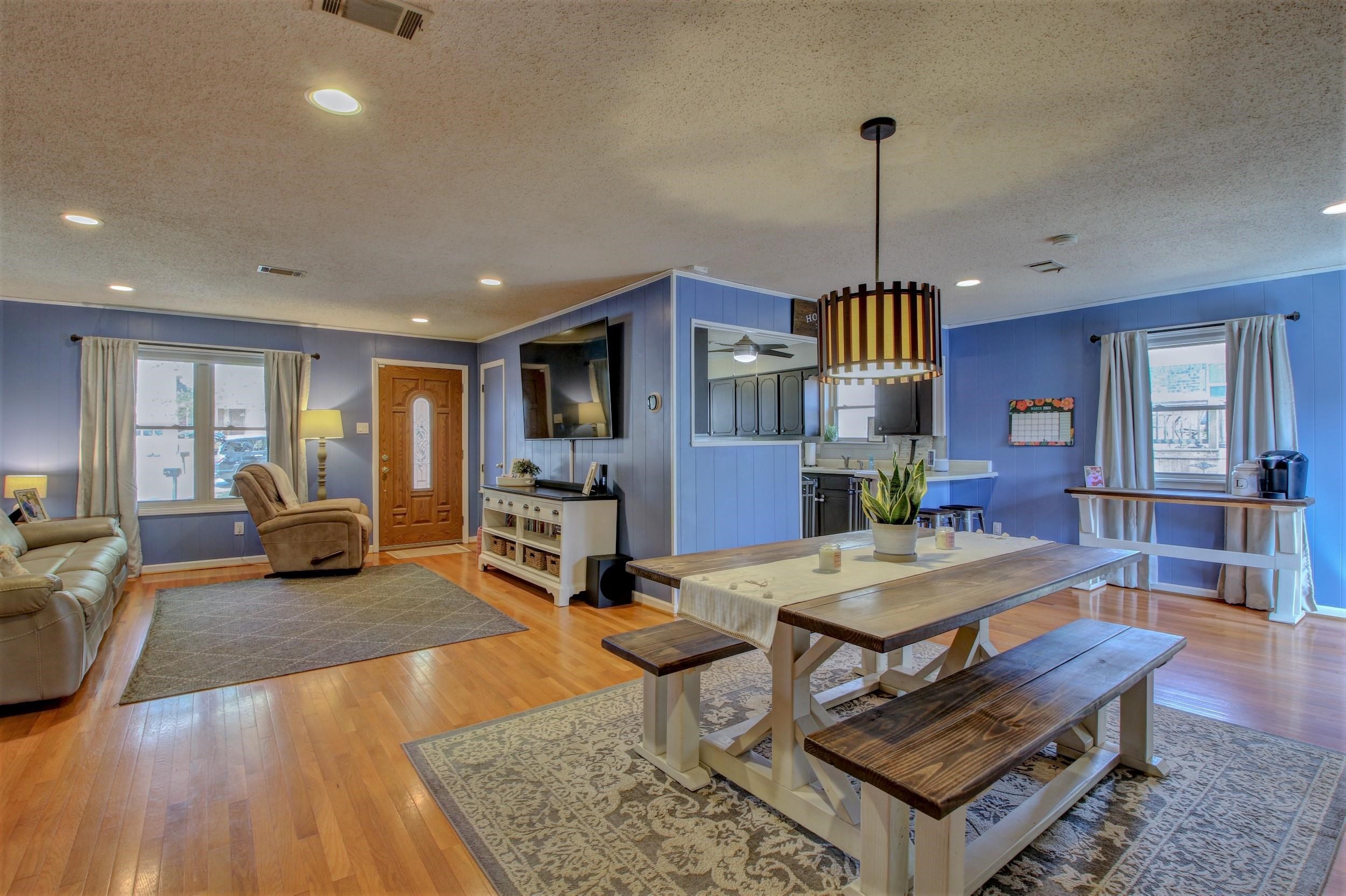 Open-plan living and dining room with blue walls, hardwood floors, and a large wooden table with benches.